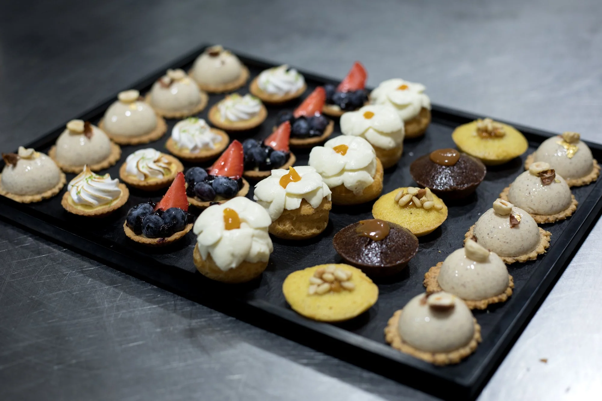 Plateau de diverses petites pâtisseries décorées avec fruits, crèmes, et chocolats.
