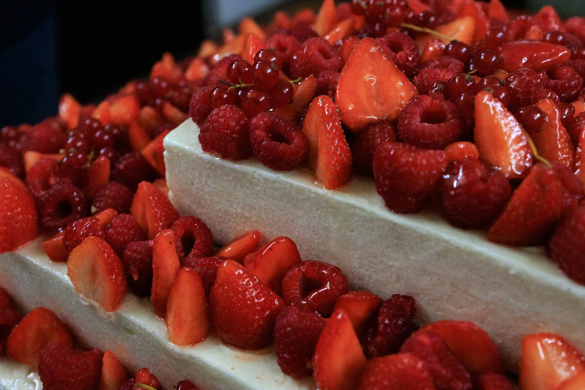 Gros plan sur un gâteau blanc à étages décoré de fraises, framboises et groseilles.