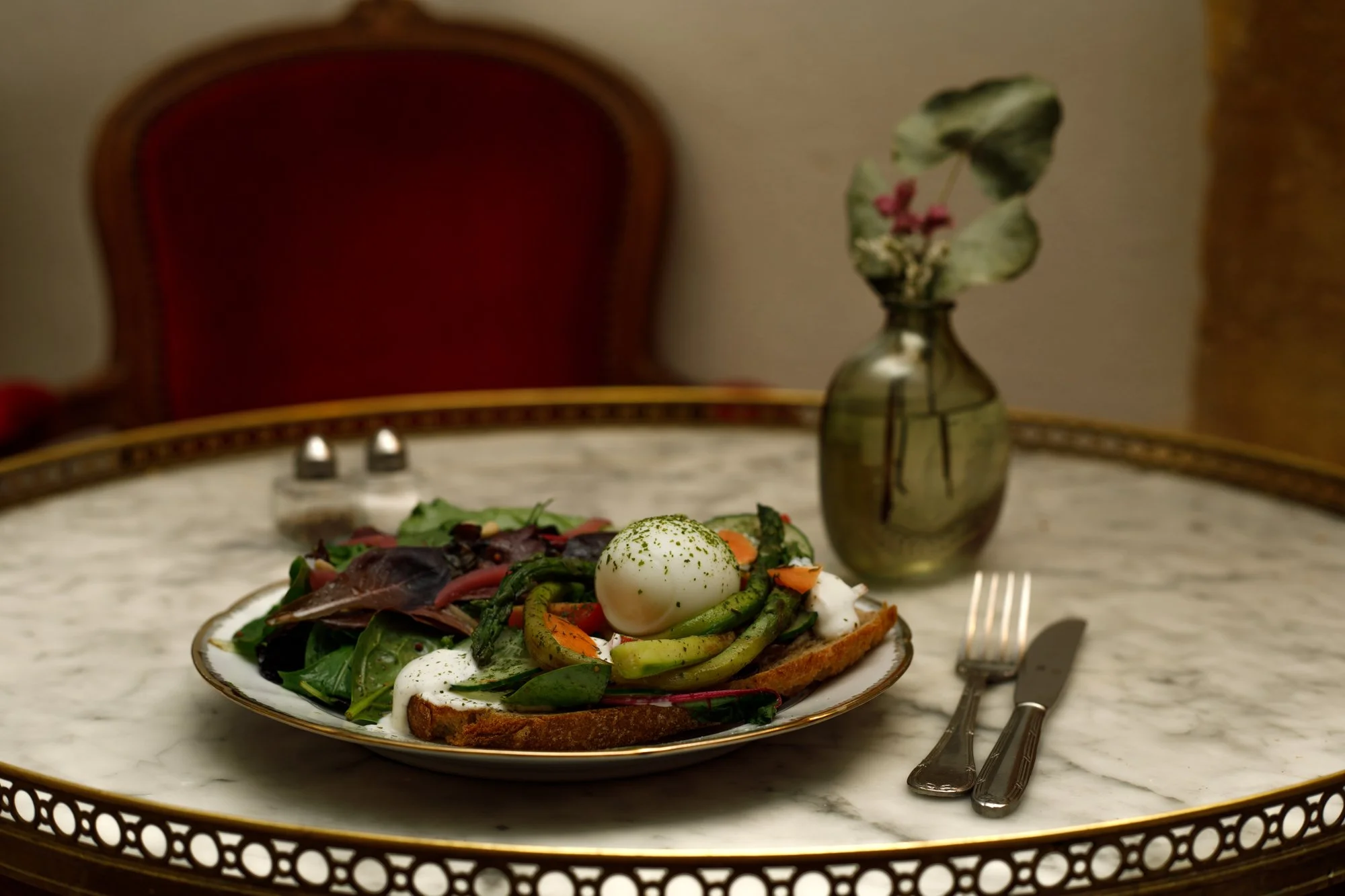 Tartine aux asperges et oeuf accompagnée de salade sur une assiette en porcelaine déposée sur une table bouillote devant un fauteuil Louis XV à la pâtisserie Chez Apolline