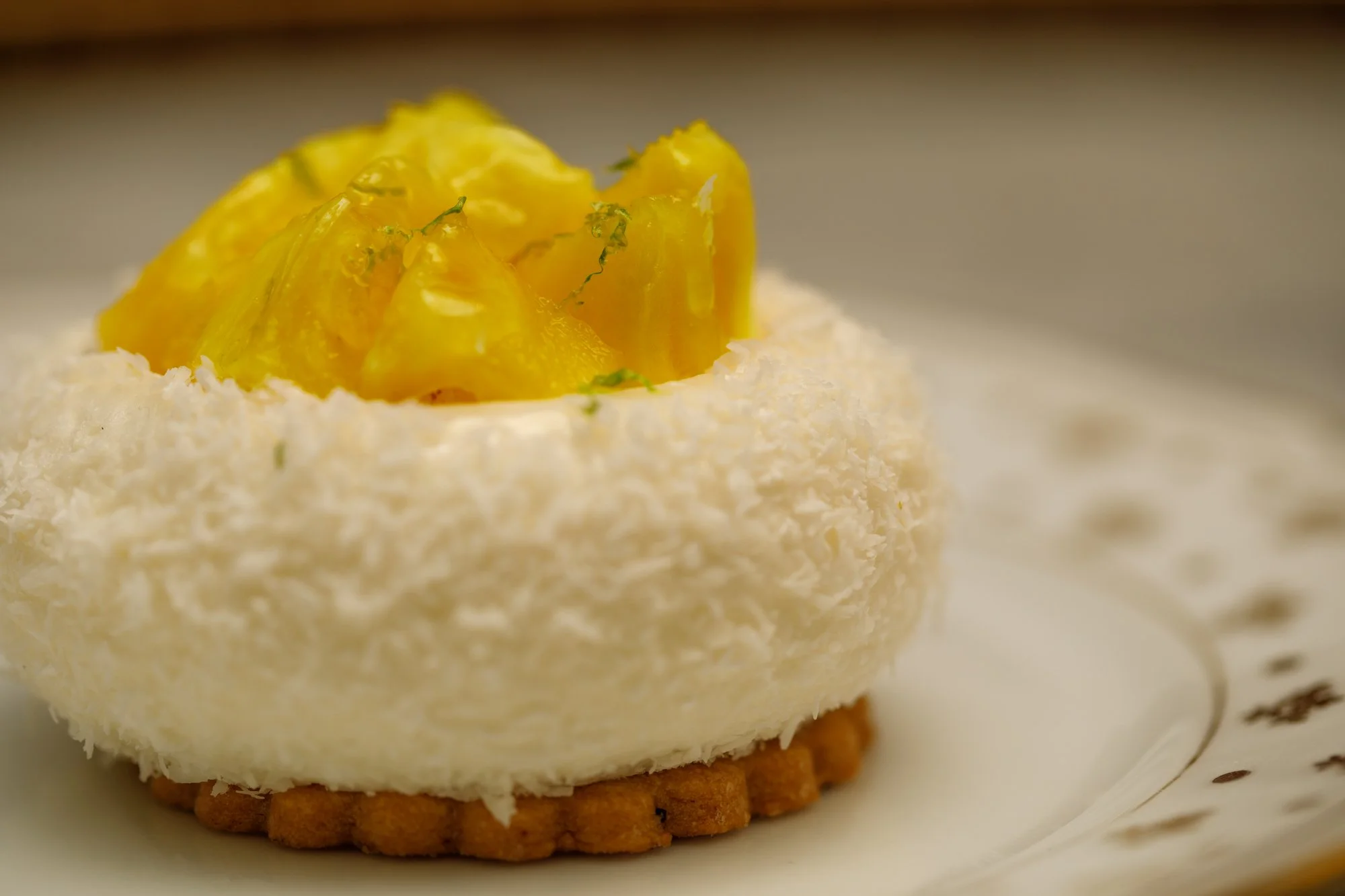 Entremet à la noix de coco sur un sablé et surmonté d'ananas coupé, le tout sur une assiette en porcelaine