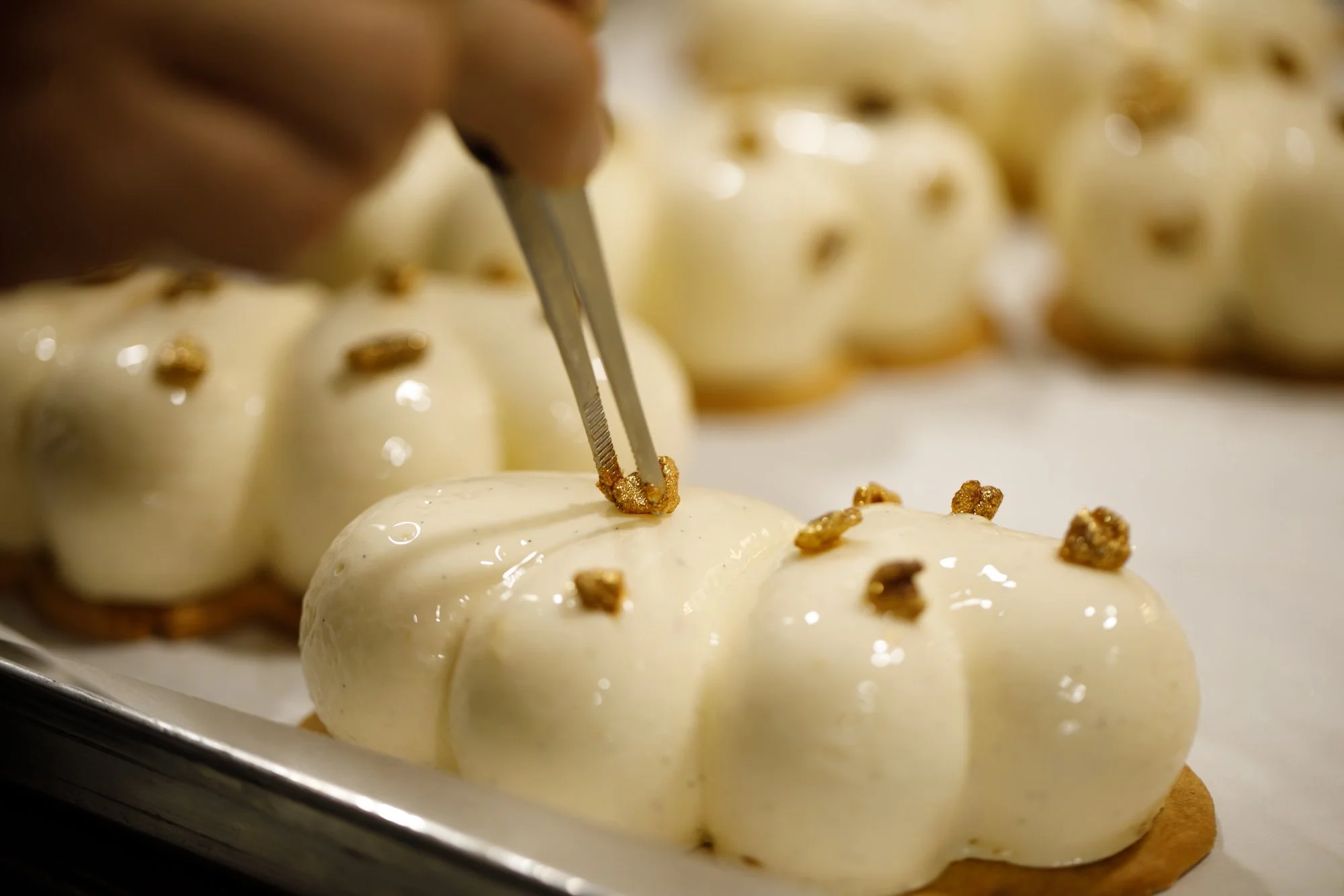 Un morceau de noix de pécan est déposée à la pince avec minutie sur un entremet vanille pécan