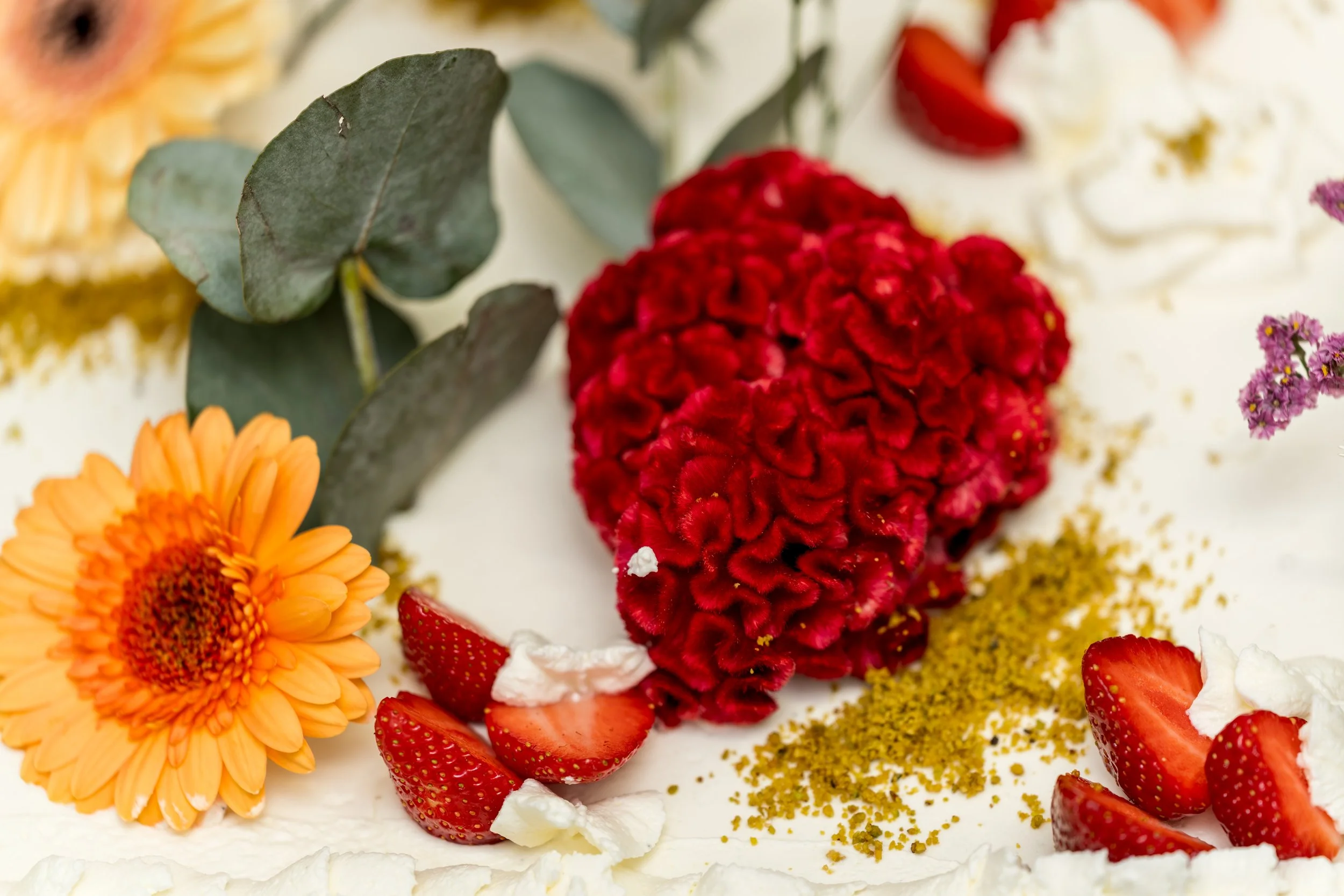 Gâteau décoré avec des fleurs, des fraises, de la crème, et de la poudre de pistache.