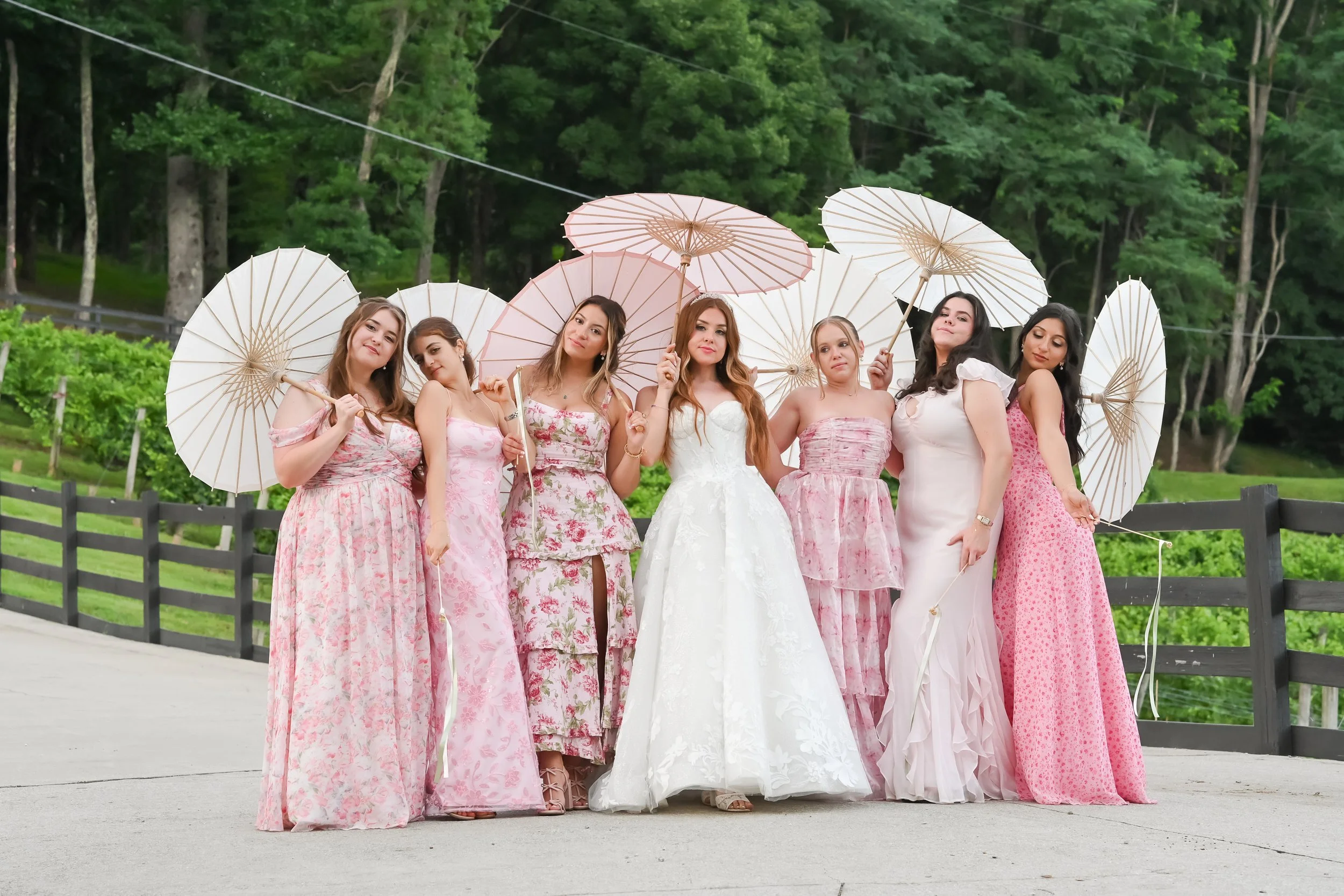Group of women in pastel-colored dresses holding paper umbrellas outdoors.