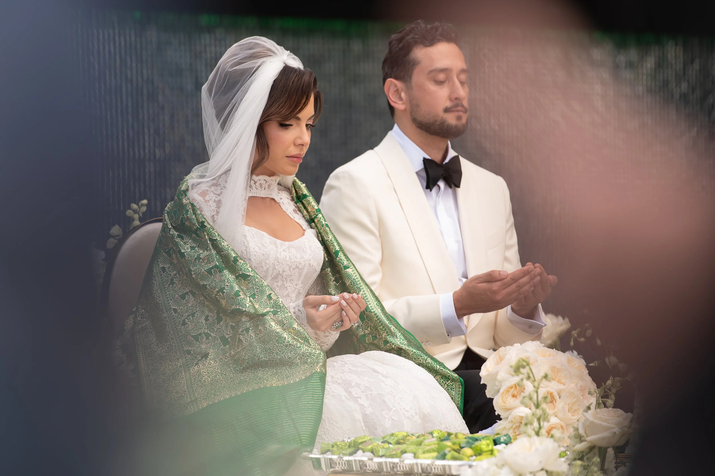 A bride and groom kneeling with heads bowed in prayer during their wedding ceremony.