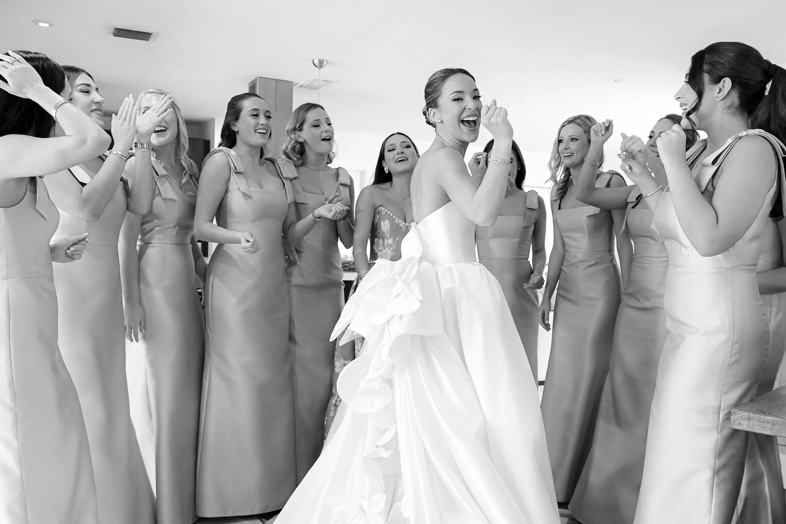 A group of women dressed in matching dresses, gathered around a bride in a wedding gown, laughing and celebrating indoors.