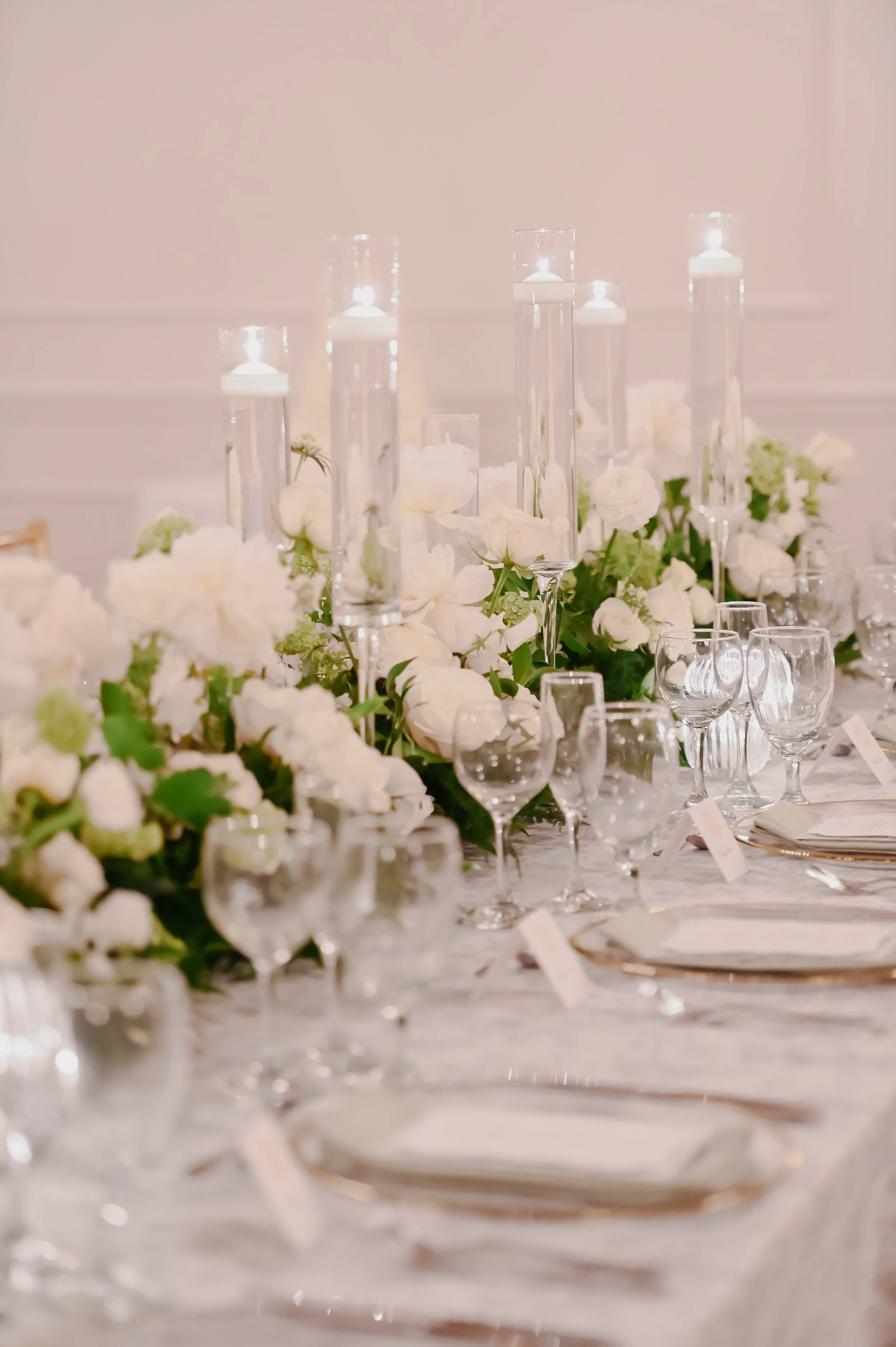 A close-up of a wedding reception table with floral arrangements and floating candles in tall, clear glass holders.