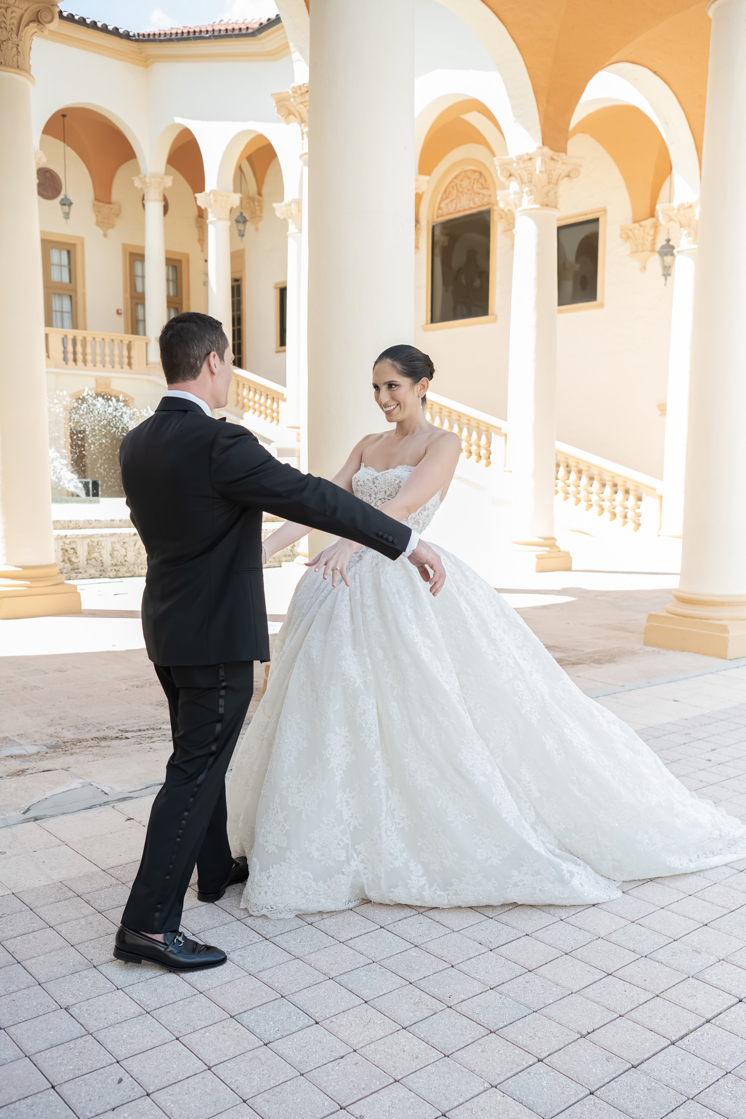 A bride and groom dancing outside a Mediterranean-style building with columns and arches.