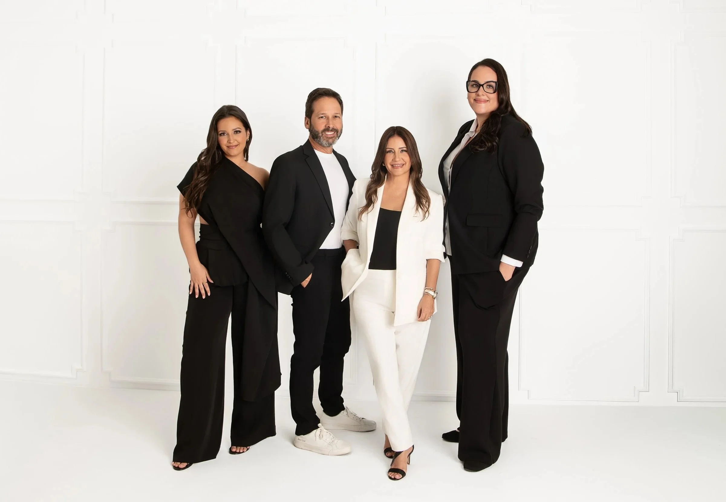Group of five professionally dressed individuals standing against a white background, smiling at the camera.
