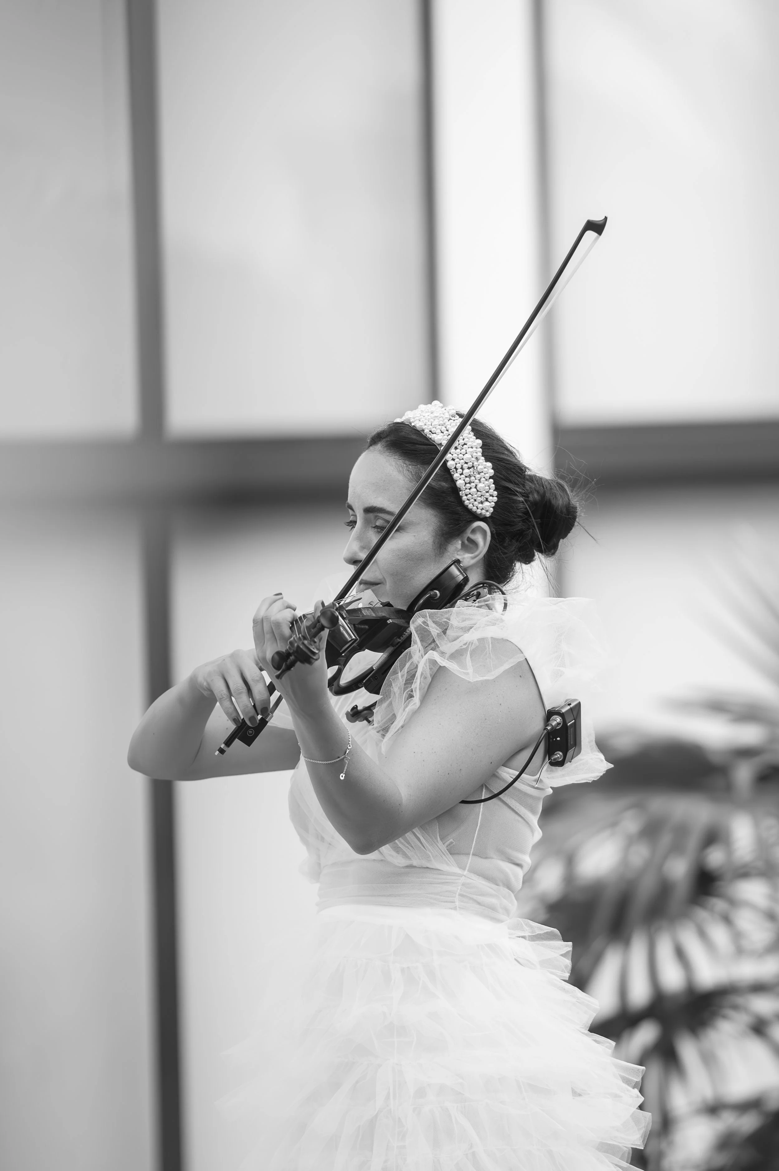 A woman in a formal dress and pearl headpiece playing the violin, with her eyes closed and a calm expression.