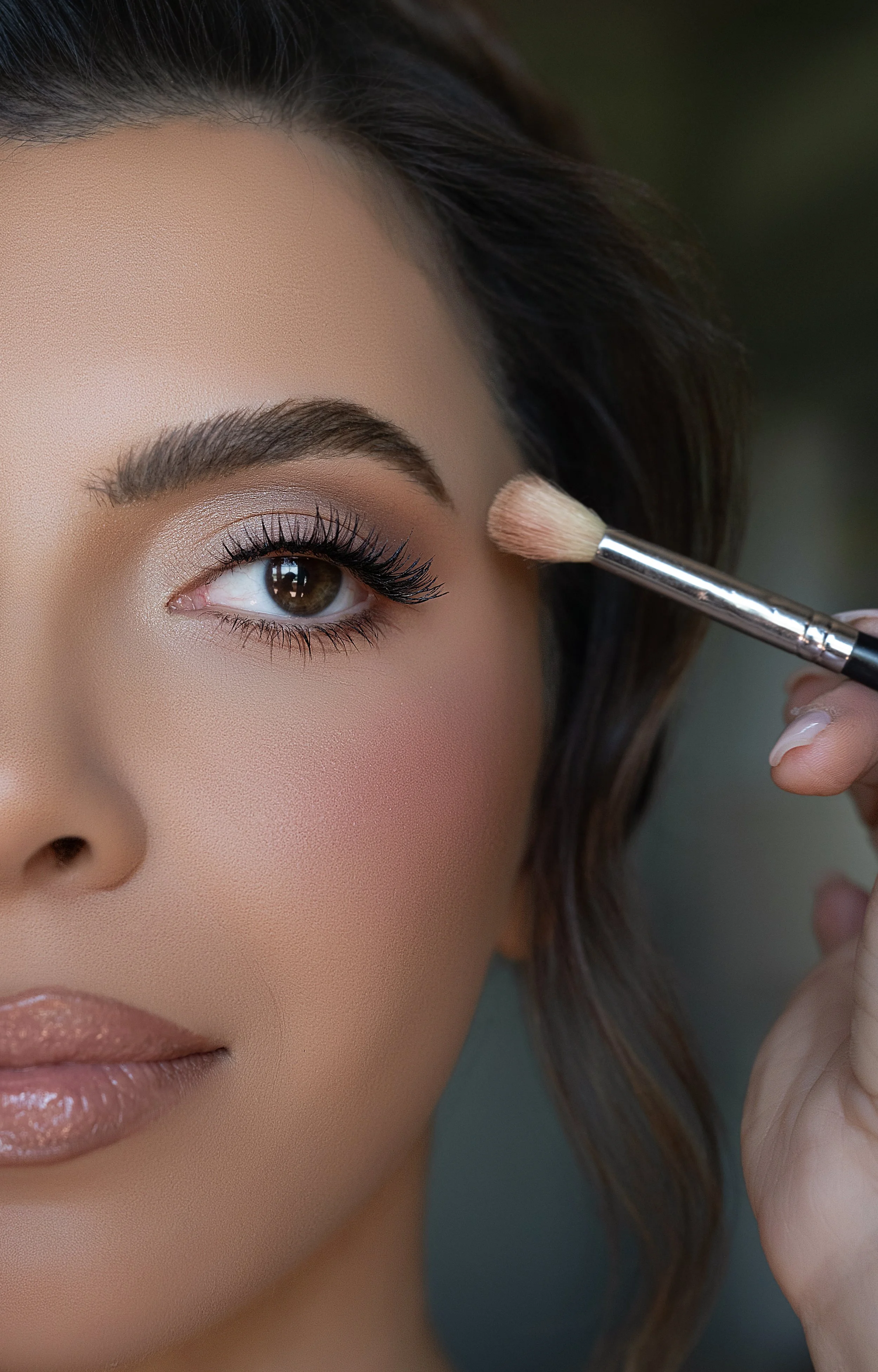 A woman receiving makeup application, with focus on her eye and a brush near her eyelid.
