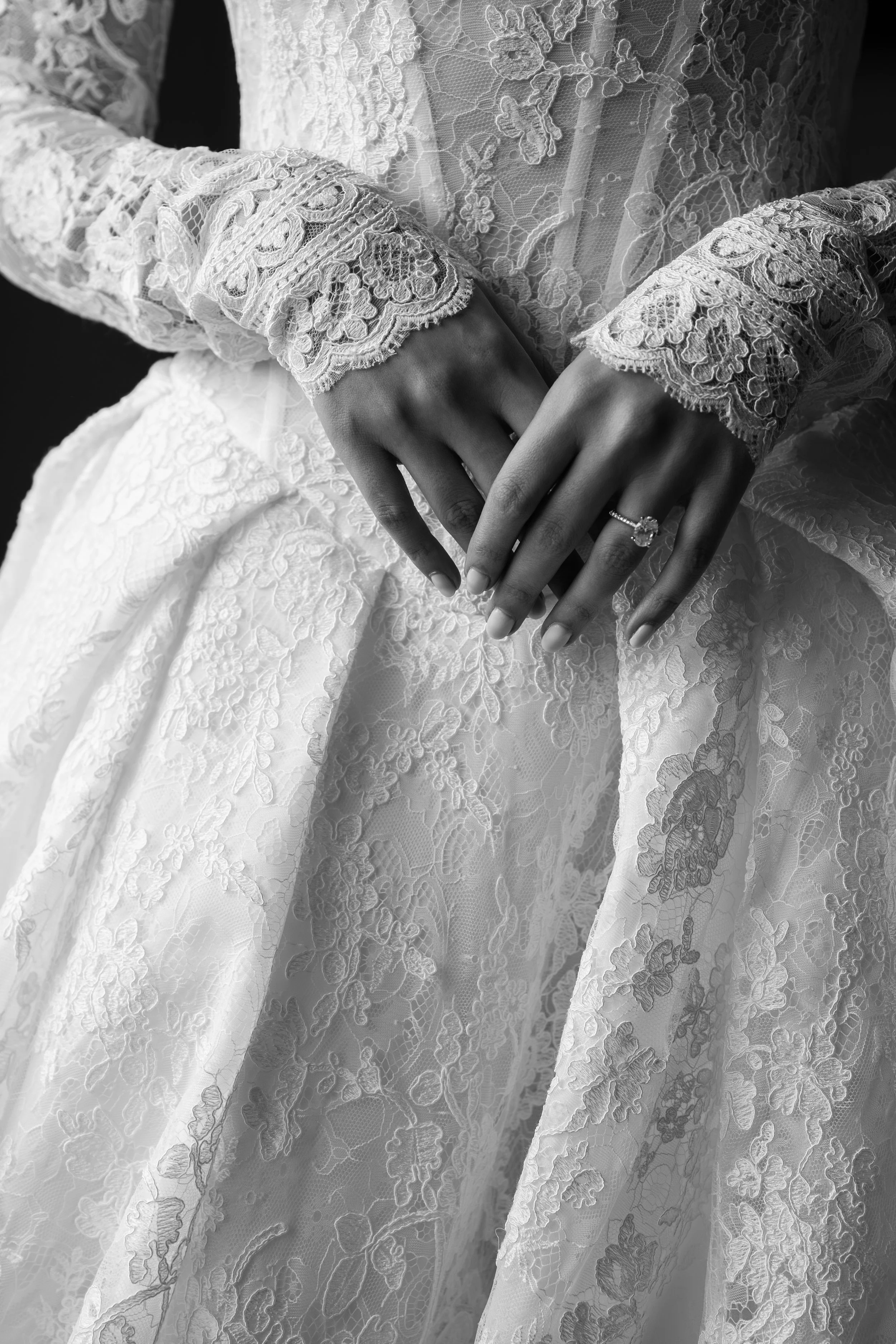 Close-up of a person wearing a lace dress, showcasing intricate lace detailing on the long sleeves and fabric, with a ring on the left hand.