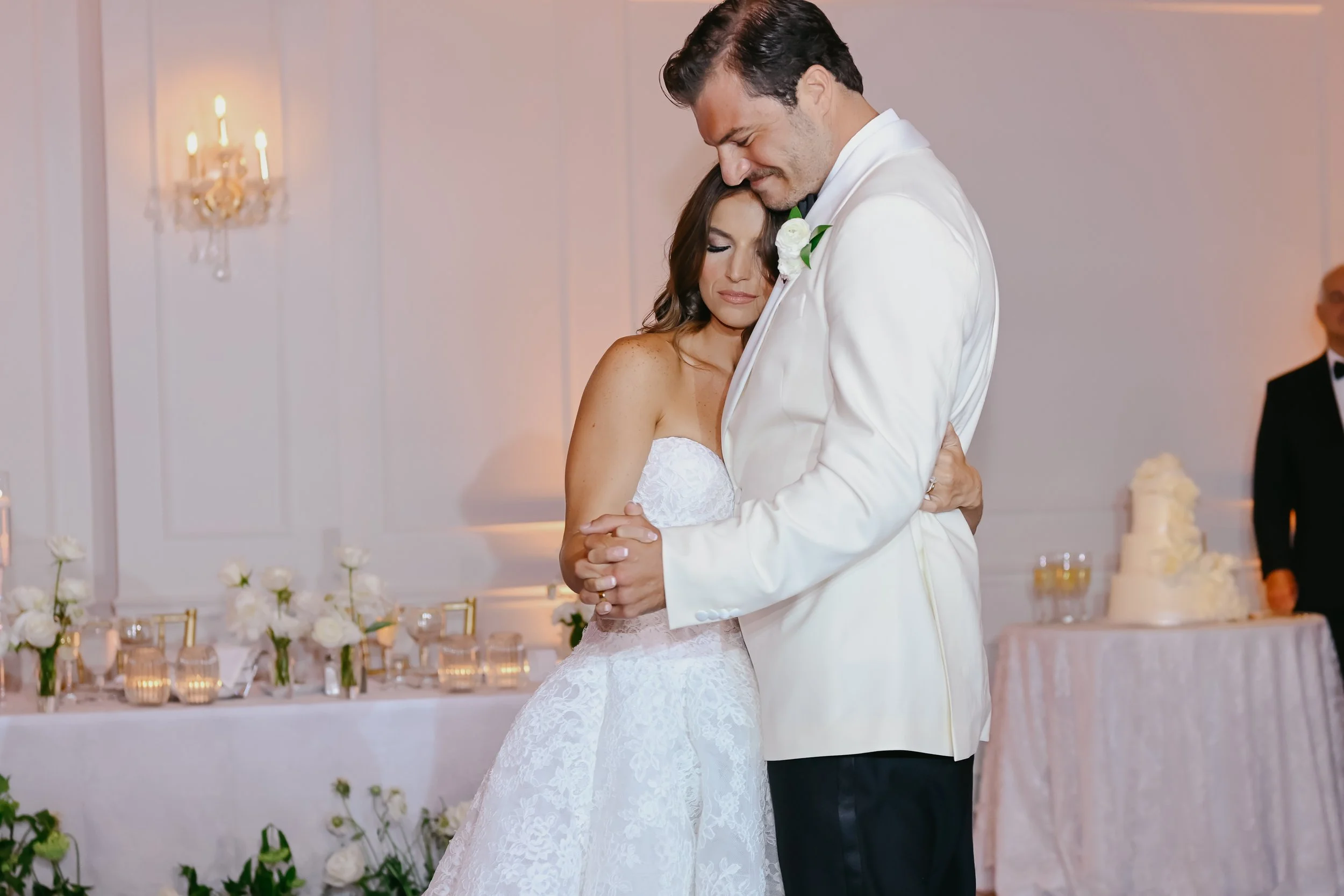 A bride and groom sharing a dance at their wedding reception, with floral decorations and candles in the background.