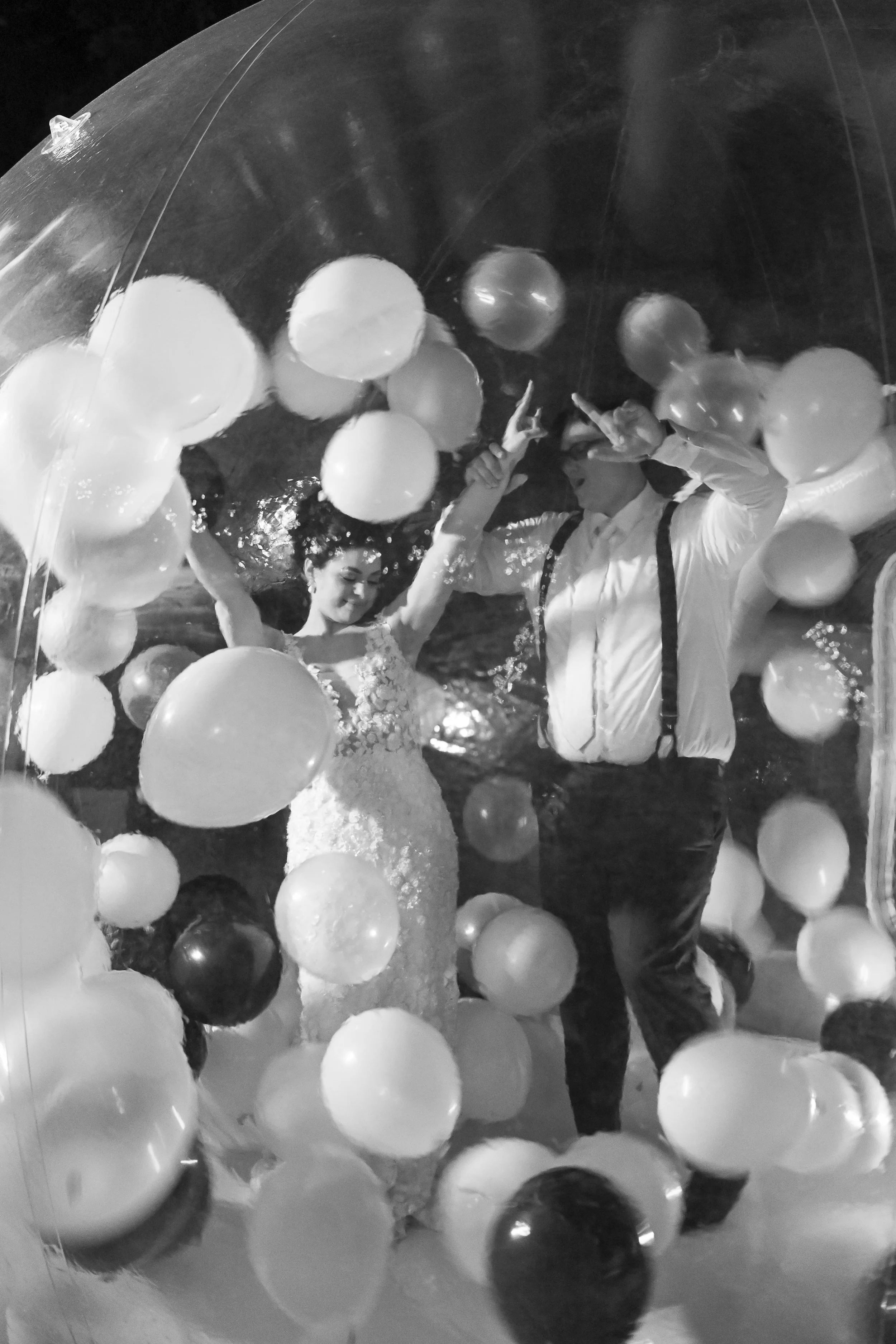 People holding balloons inside a transparent inflatable structure, celebrating together at night.