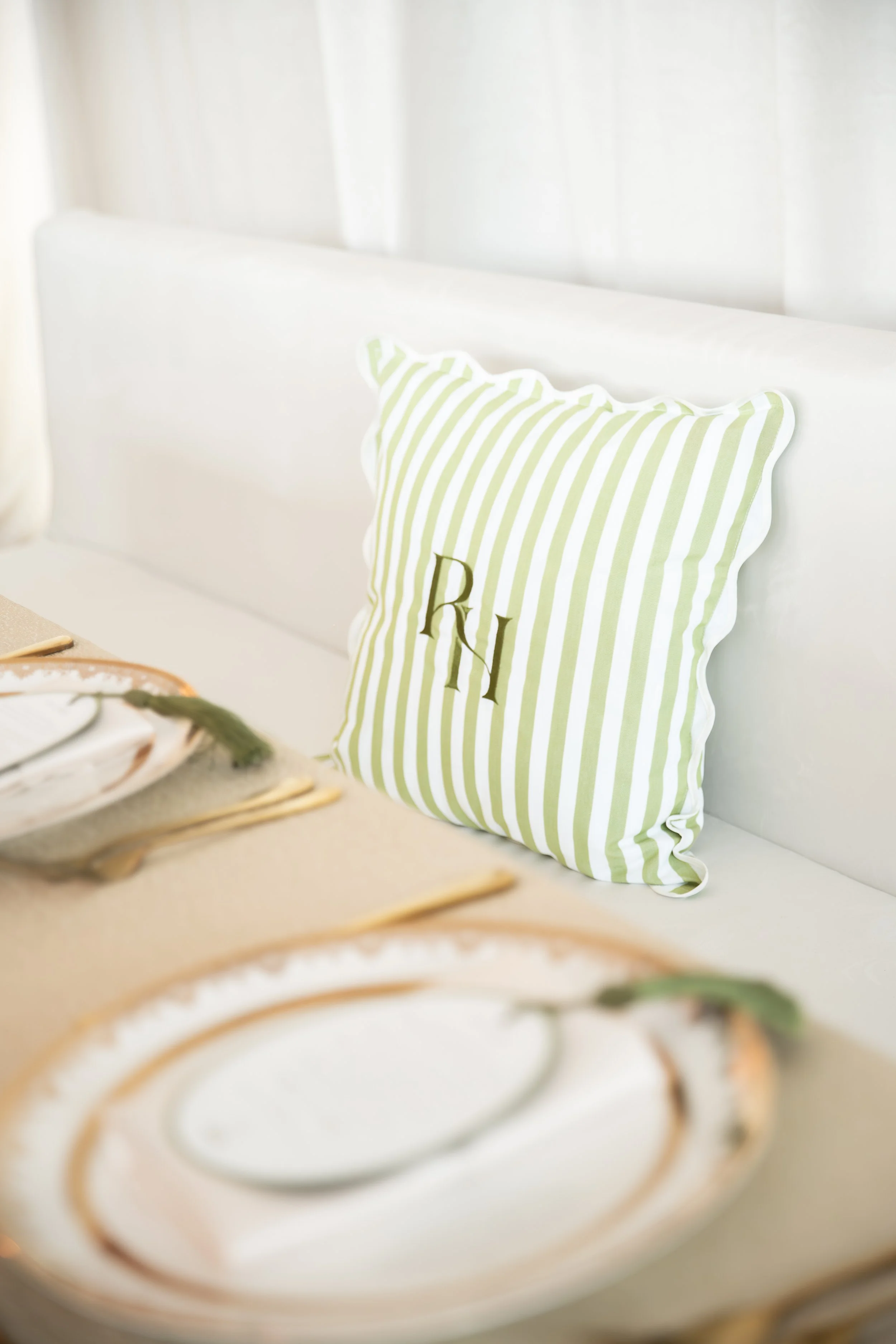 Close-up of a plate with a dessert garnished with a drizzle of caramel and a mint sprig, with a blurry patterned cake in the foreground and a green and white striped pillow with initials in the background.