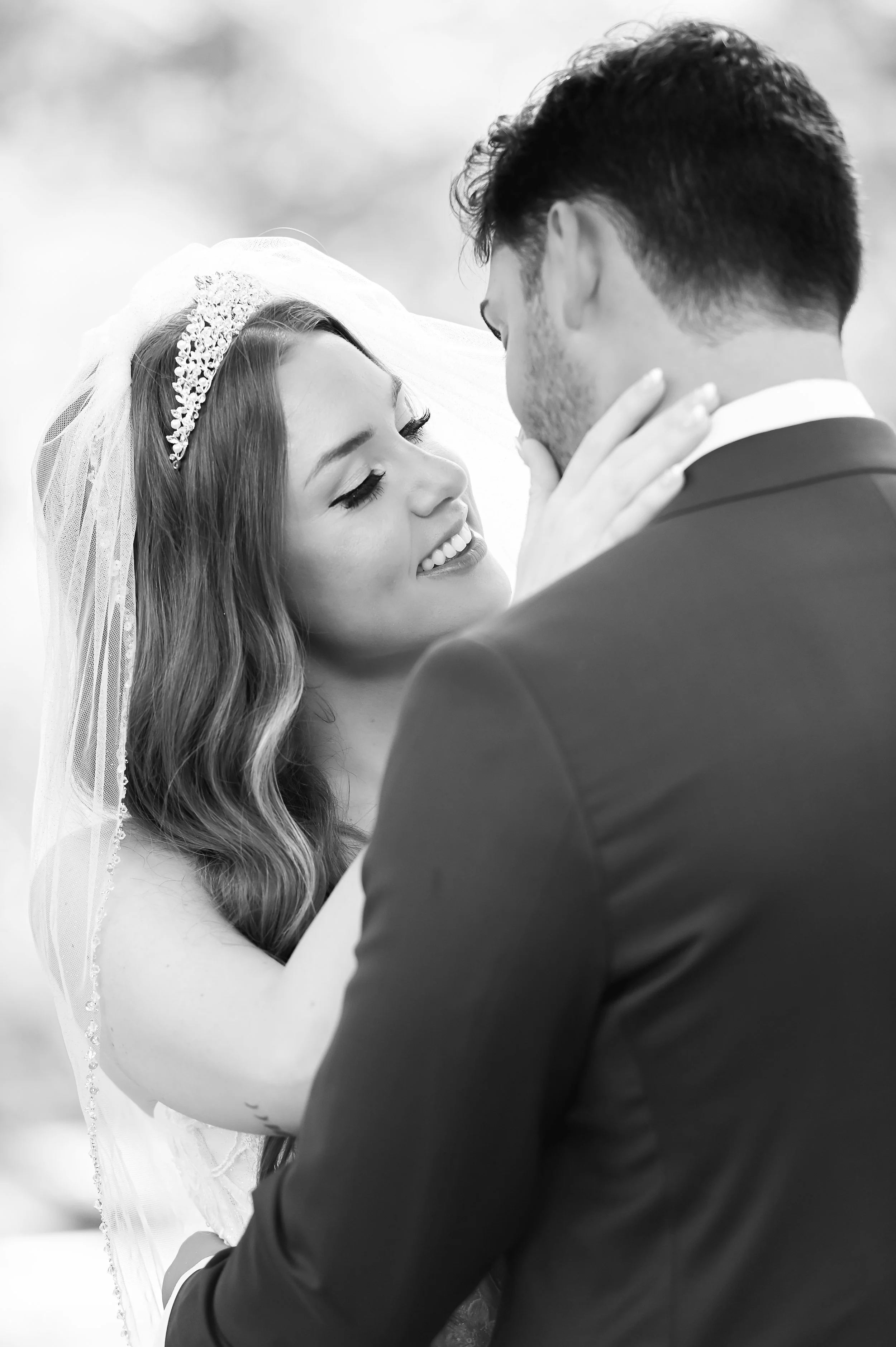 A bride and groom sharing a kiss during their wedding ceremony, with the bride smiling and wearing a white gown and a tiara, and the groom in a dark suit.