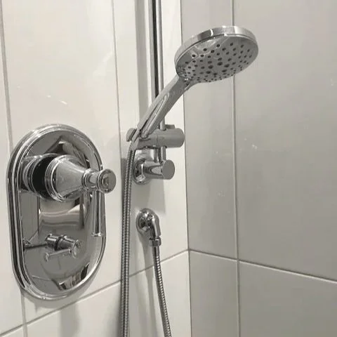 A chrome showerhead attached to a wall with a flexible hose, mounted inside a tiled shower
