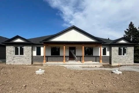 Newly constructed single-story house with front porch, wooden pillars, and multiple windows, set against a blue sky with some clouds, with bare dirt yard in front.