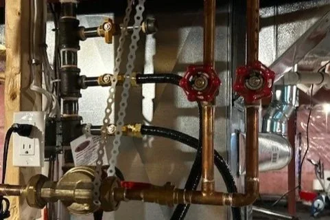 Close-up view of plumbing pipes and fixtures in a basement or utility room.