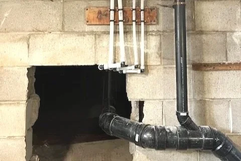 Indoor utility area with exposed pipes and a square hole in the wall.