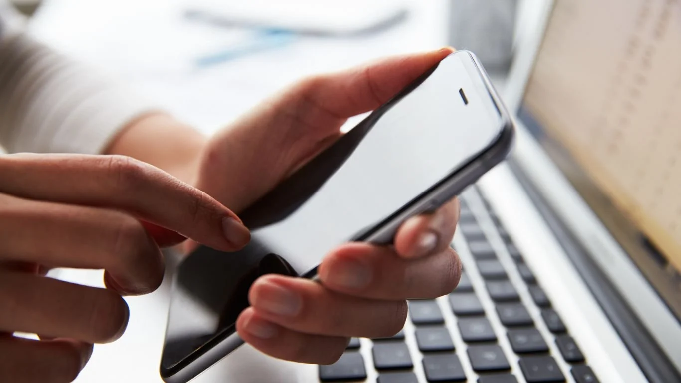 A person holds their mobile device and uses their finger to touch it.