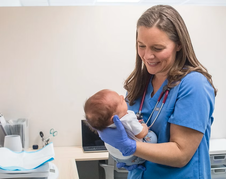 A female nurse holding a newborn baby in a medical office.