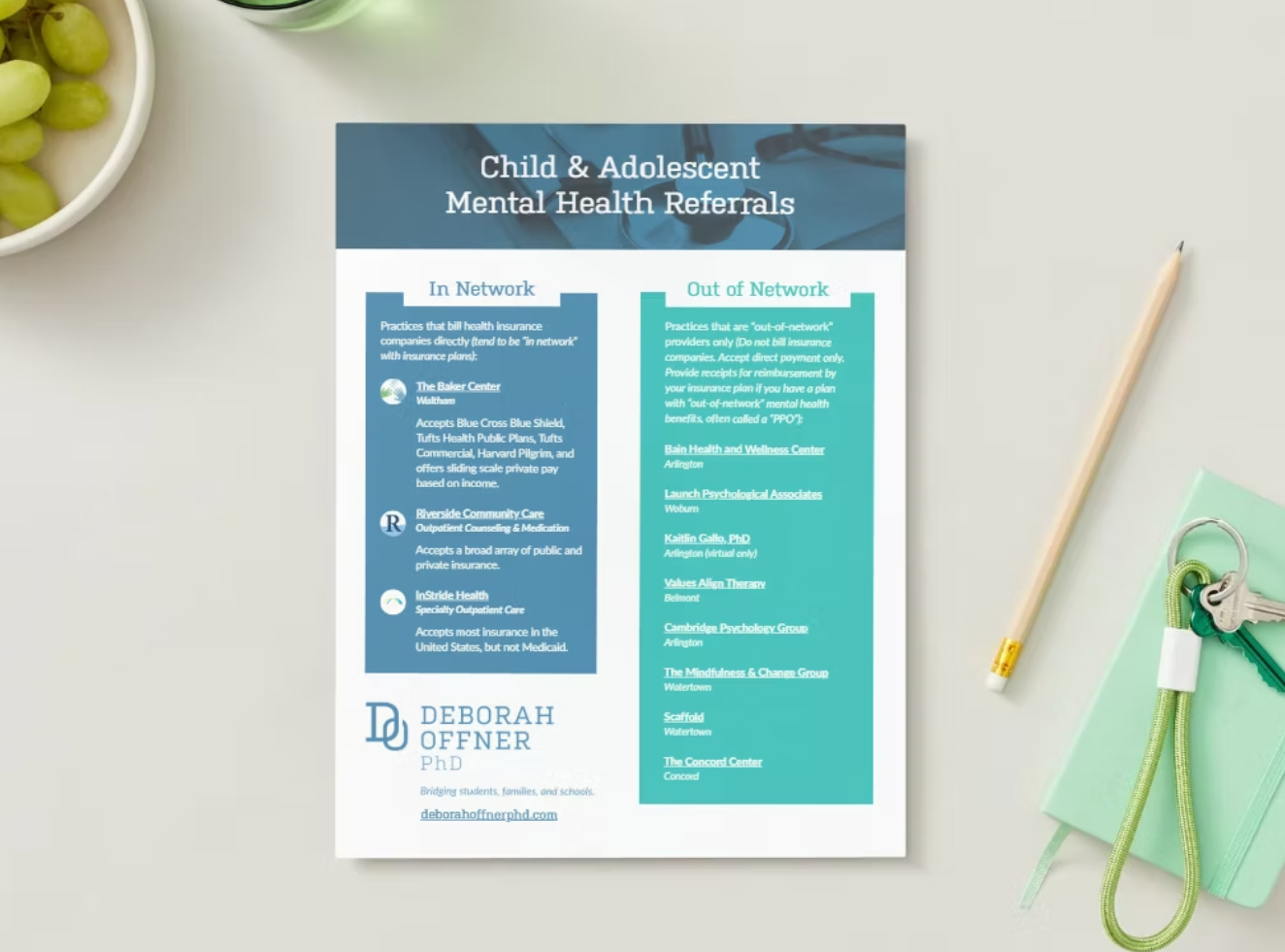 A printed flyer titled "Child & Adolescent Mental Health Referrals" with sections "In Network" and "Out of Network," listing mental health providers and features a logo, social media, and website information at the bottom. The flyer is placed on a light surface with a yellow pencil, a keychain, and a green notepad nearby, and a bowl of green grapes in the top left corner.