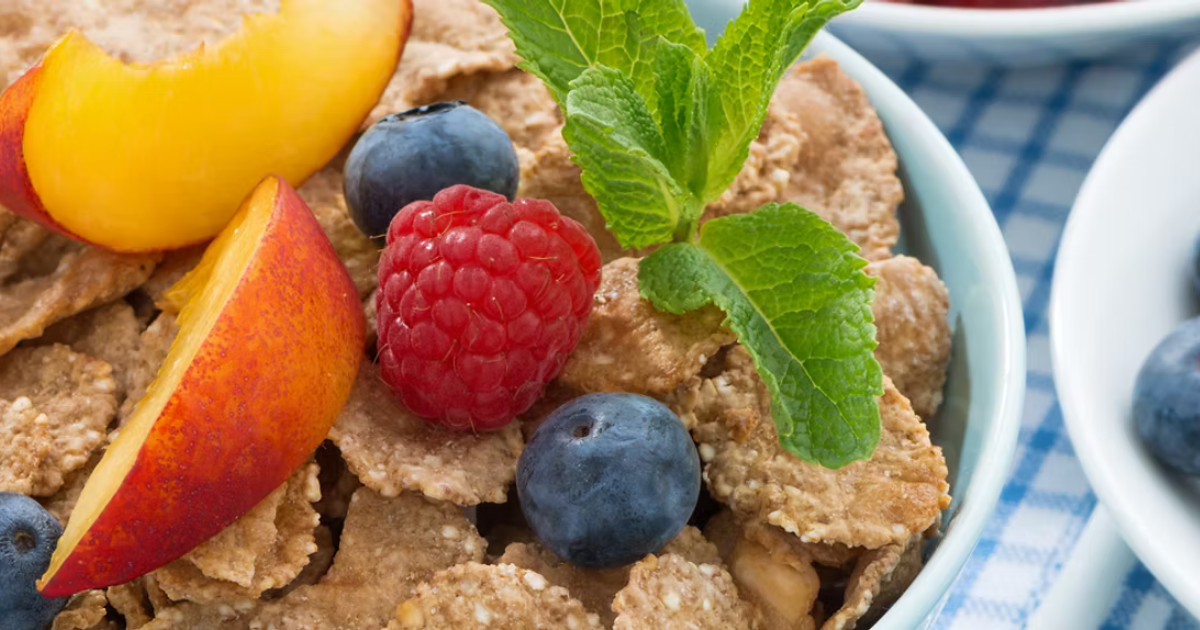 Close-up of a bowl of cereal with fresh berries, peach slices, and mint leaves on top.
