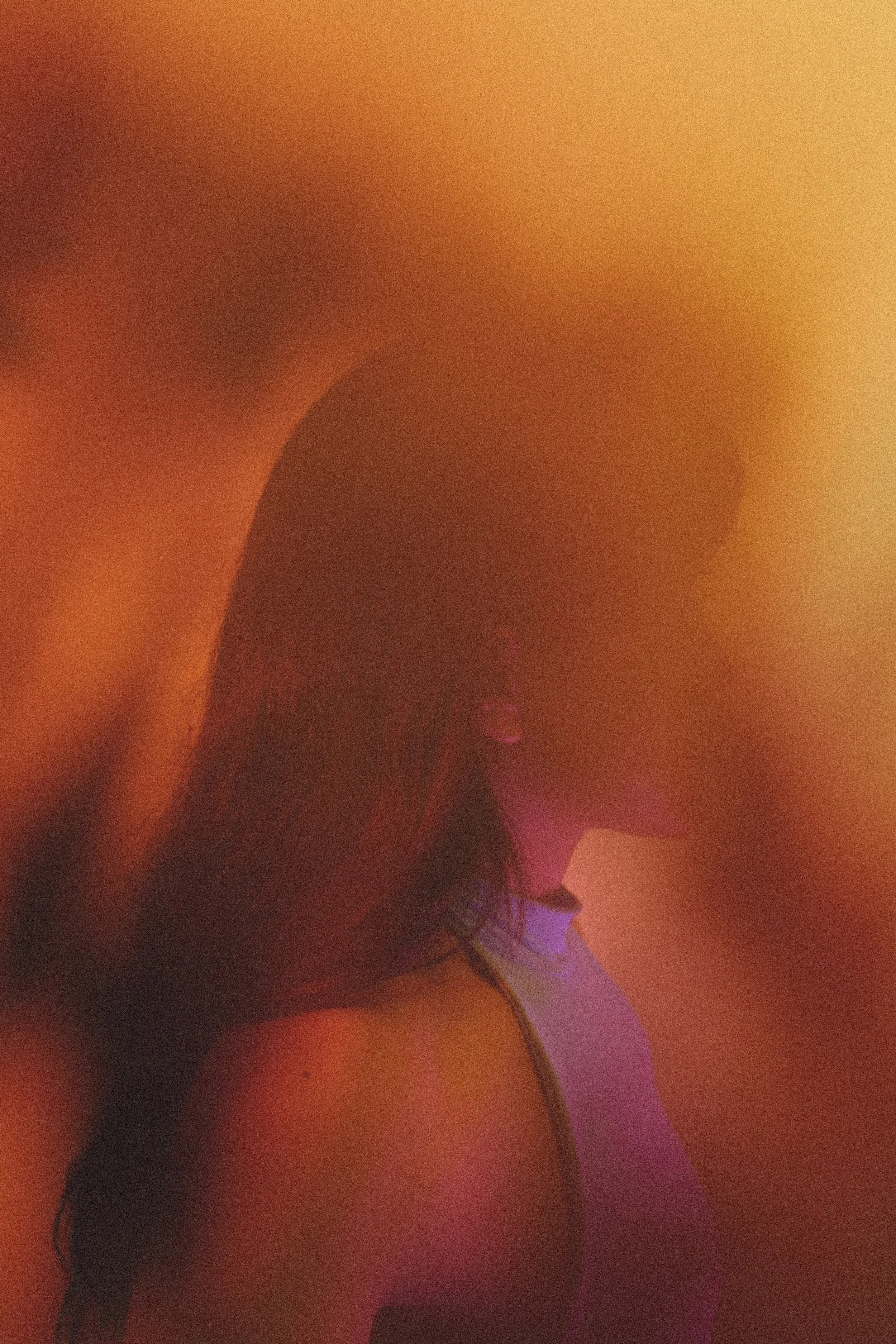 A person with long dark hair and a string top in a dimly lit room with colorful lights, creating a blurry and abstract appearance.
