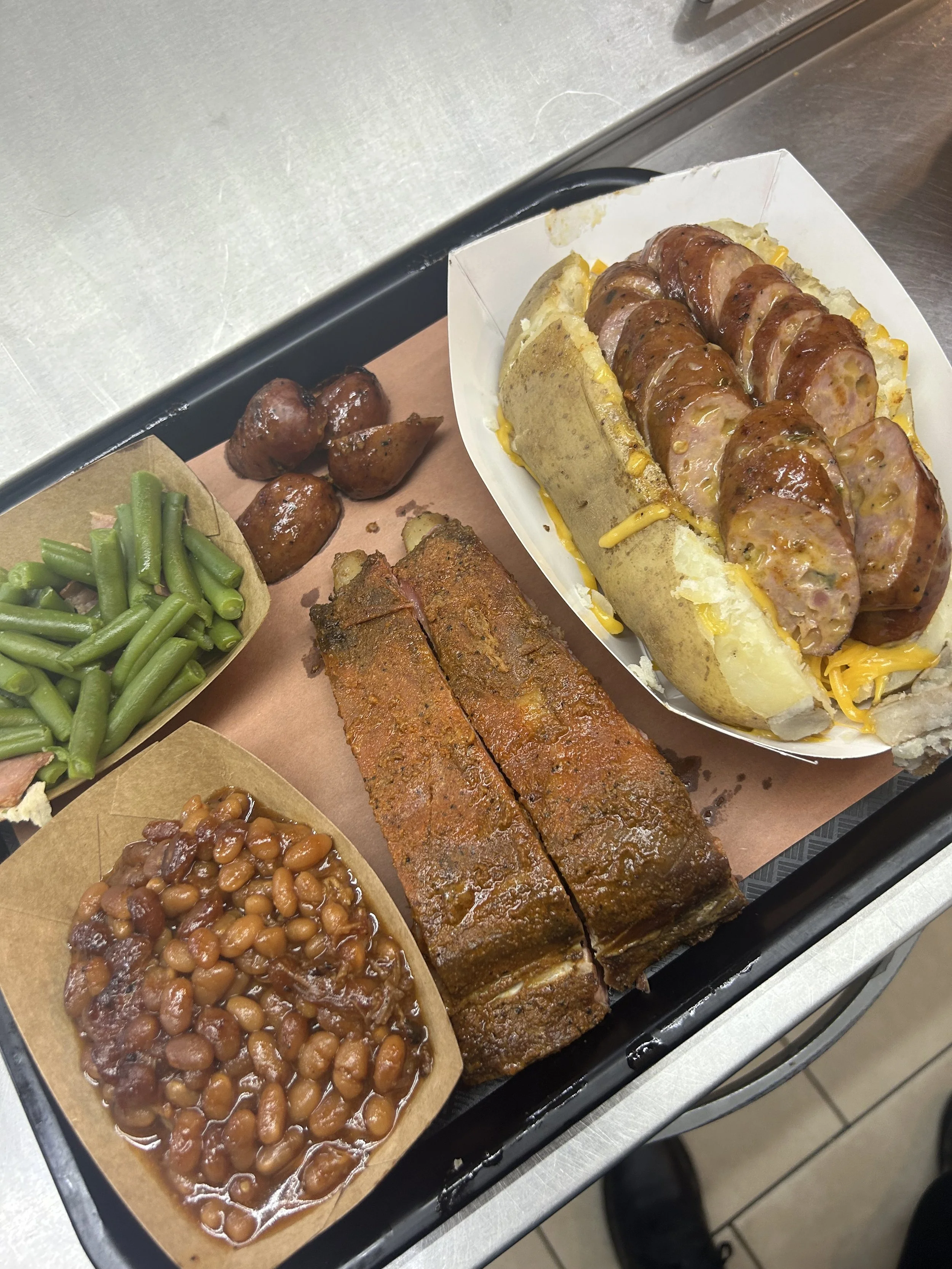 Tray of baked beans, green beans, barbecue ribs, and sliced sausage on a catering tray.