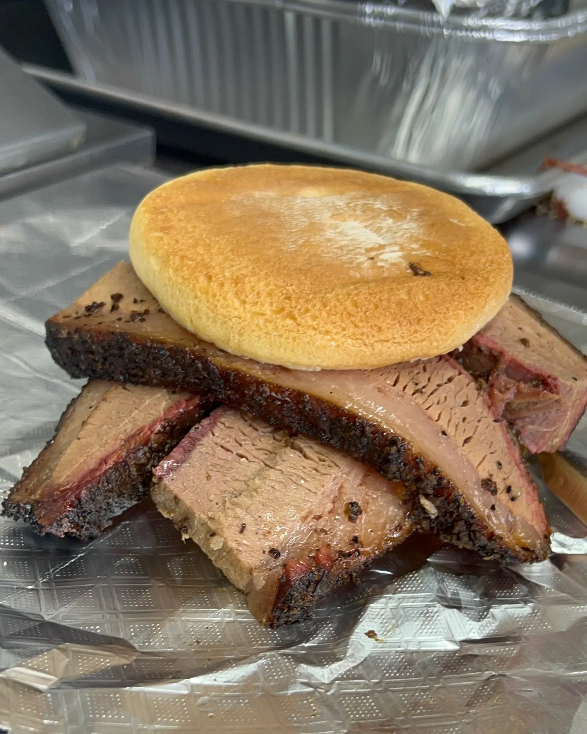 A sliced barbecue brisket sandwich, placed on a sheet of foil.