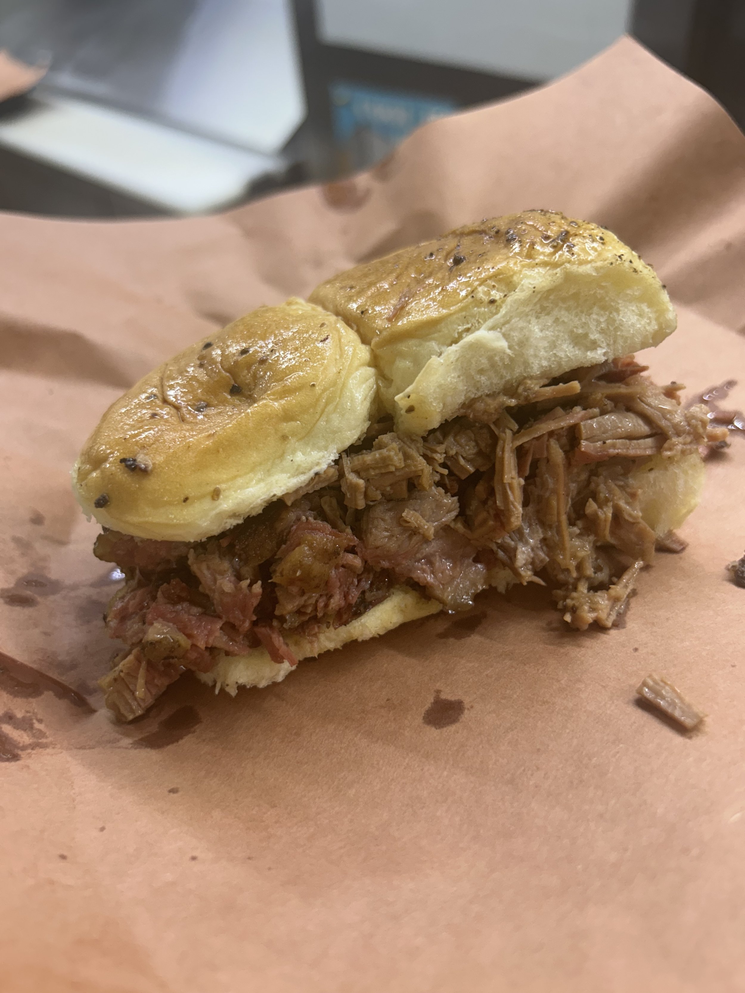 A sandwich with shredded meat and barbecue sauce on a bun, placed on brown parchment paper.