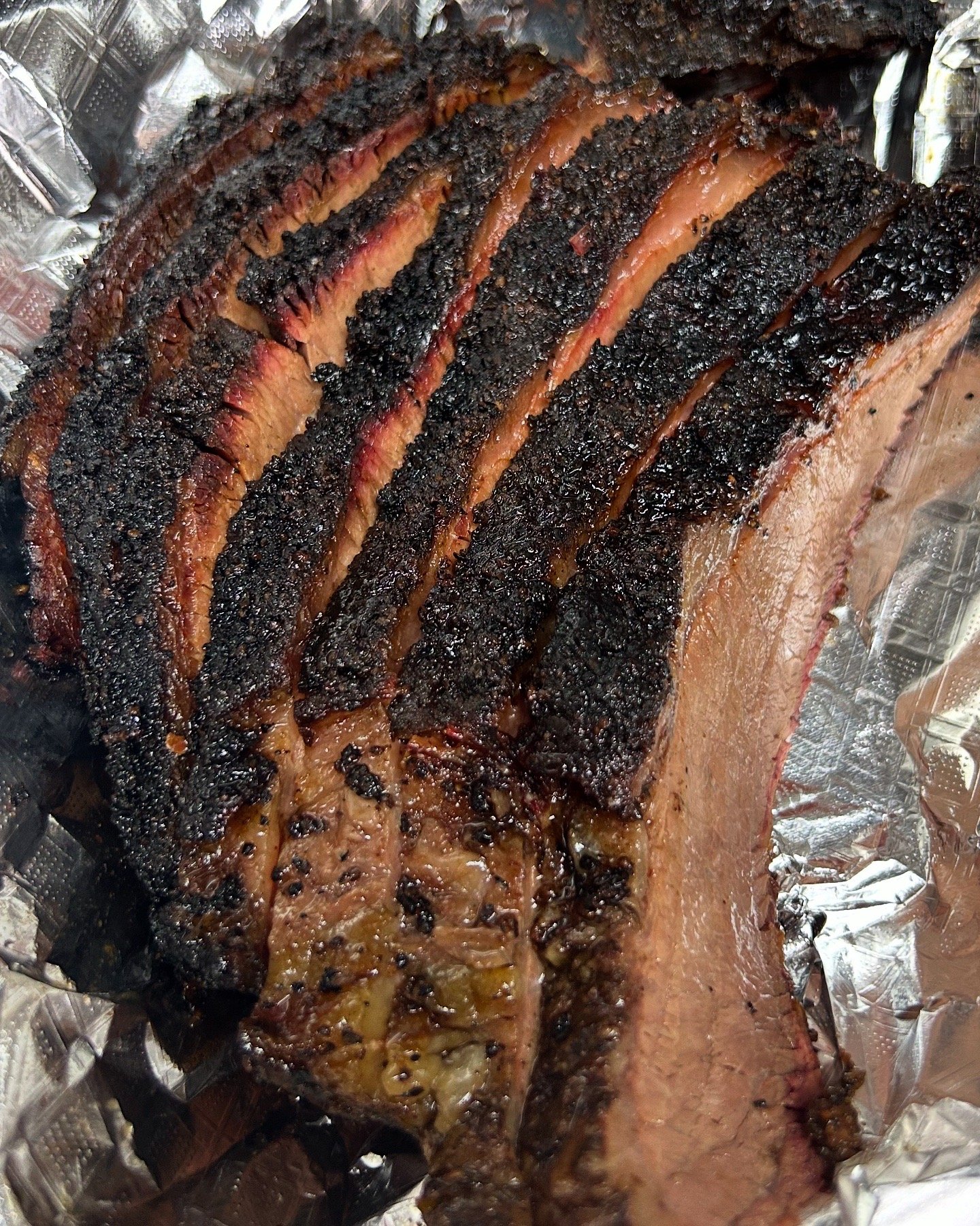Ribs with a caramelized, blackened crust on top, sitting on aluminum foil.