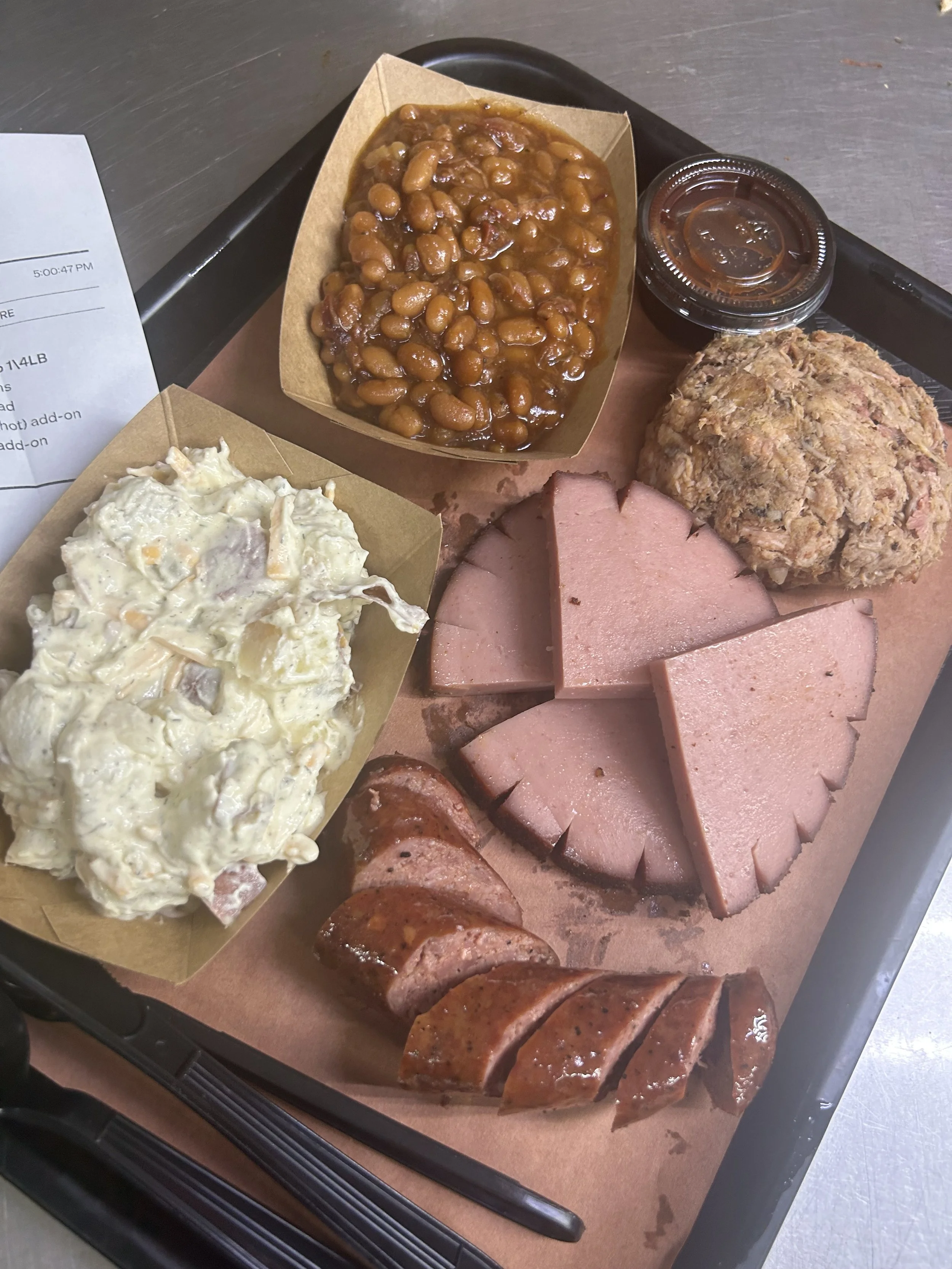 Tray with baked beans, potato salad, sliced ham, meatloaf, sliced sausage, and barbecue ribs.