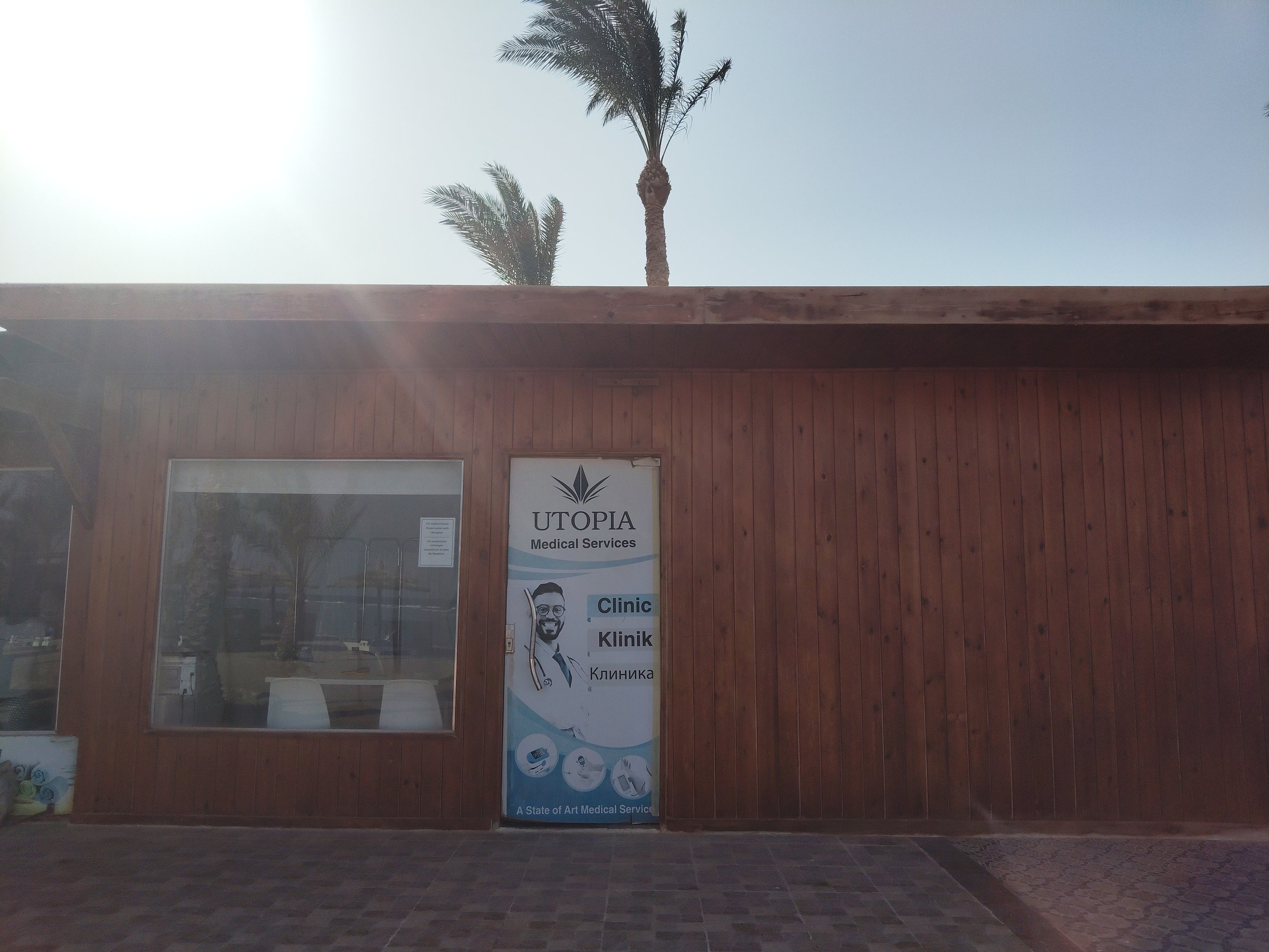 A storefront with a sign that reads 'UTOPIA Medical Services', featuring palm trees visible through the windows and doors at the entrance.