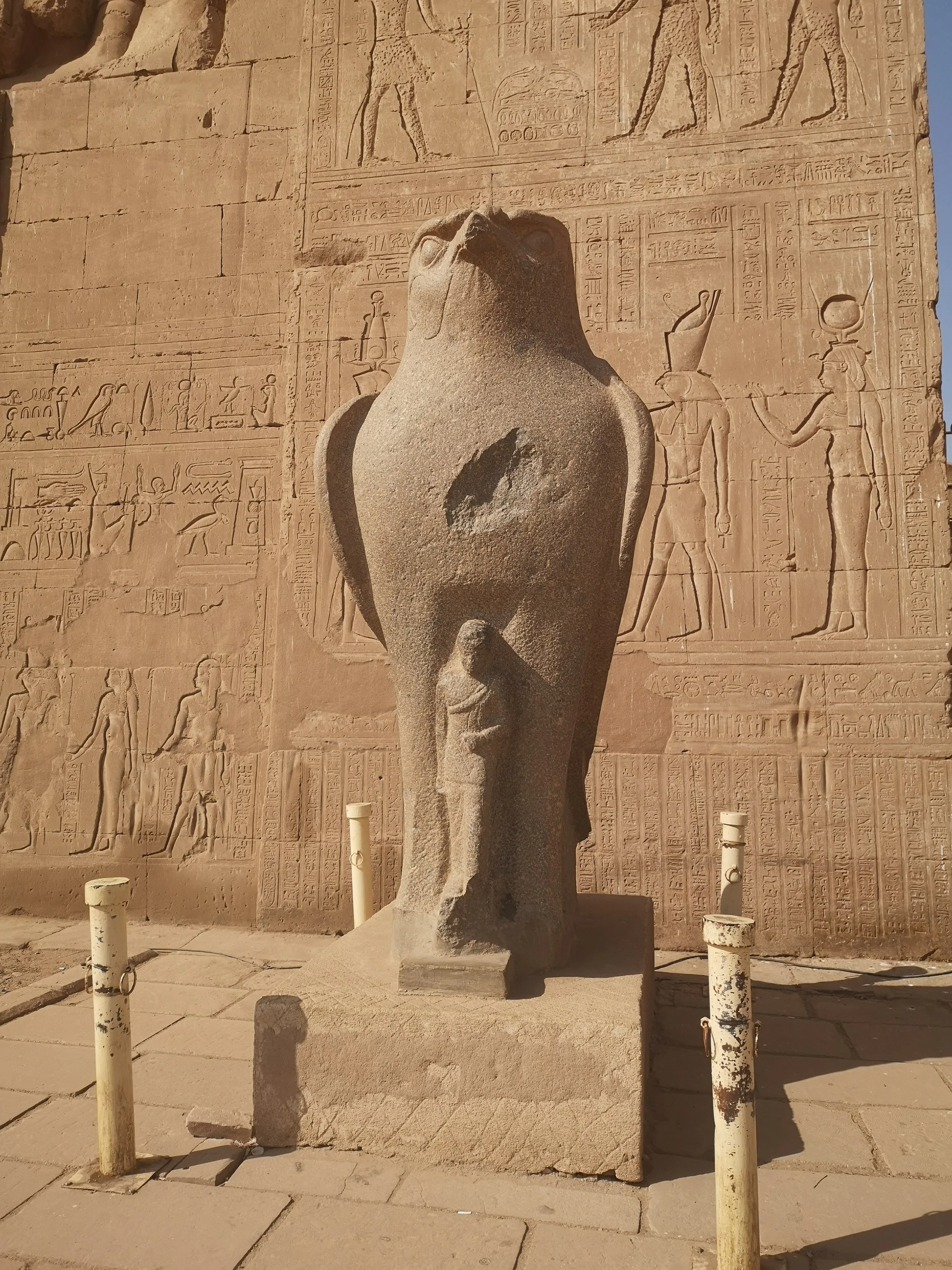 An ancient stone sculpture of a pharaoh with a missing head, placed in front of a wall covered with carved hieroglyphics and reliefs depicting Egyptian scenes.
