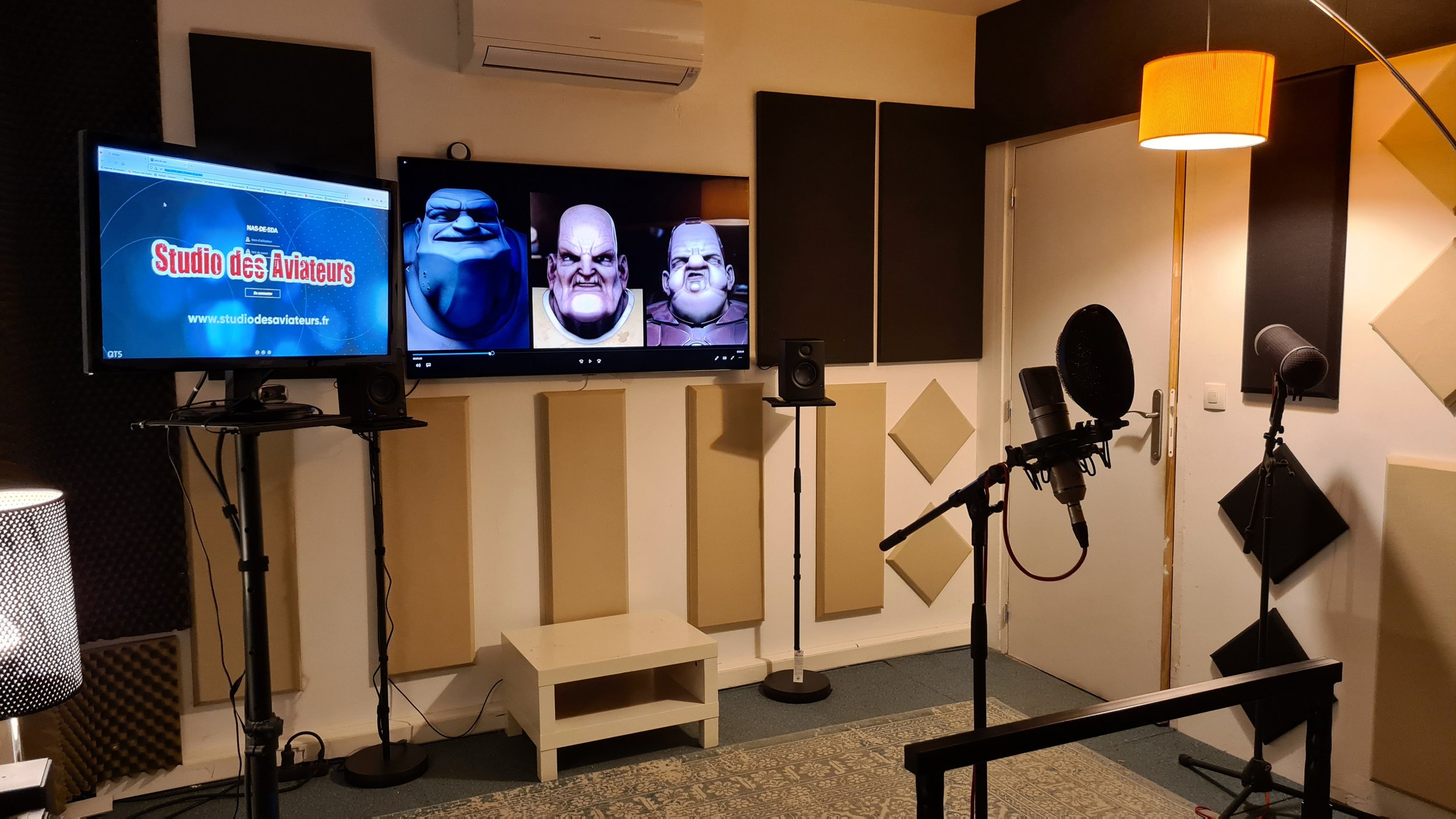 Salle de studio d'enregistrement avec microphones, écrans affichant des images de personnages animés, casques audio, lampes et panneaux d'insonorisation.