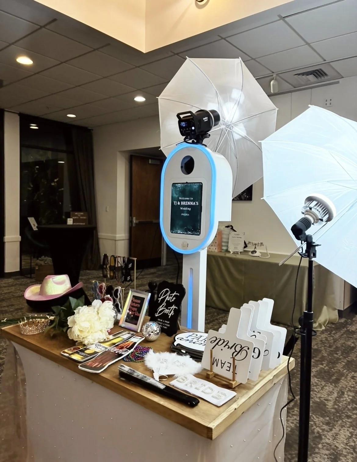 Photo booth setup at a wedding reception. Includes umbrellas, a camera, and various props and signs for taking pictures.