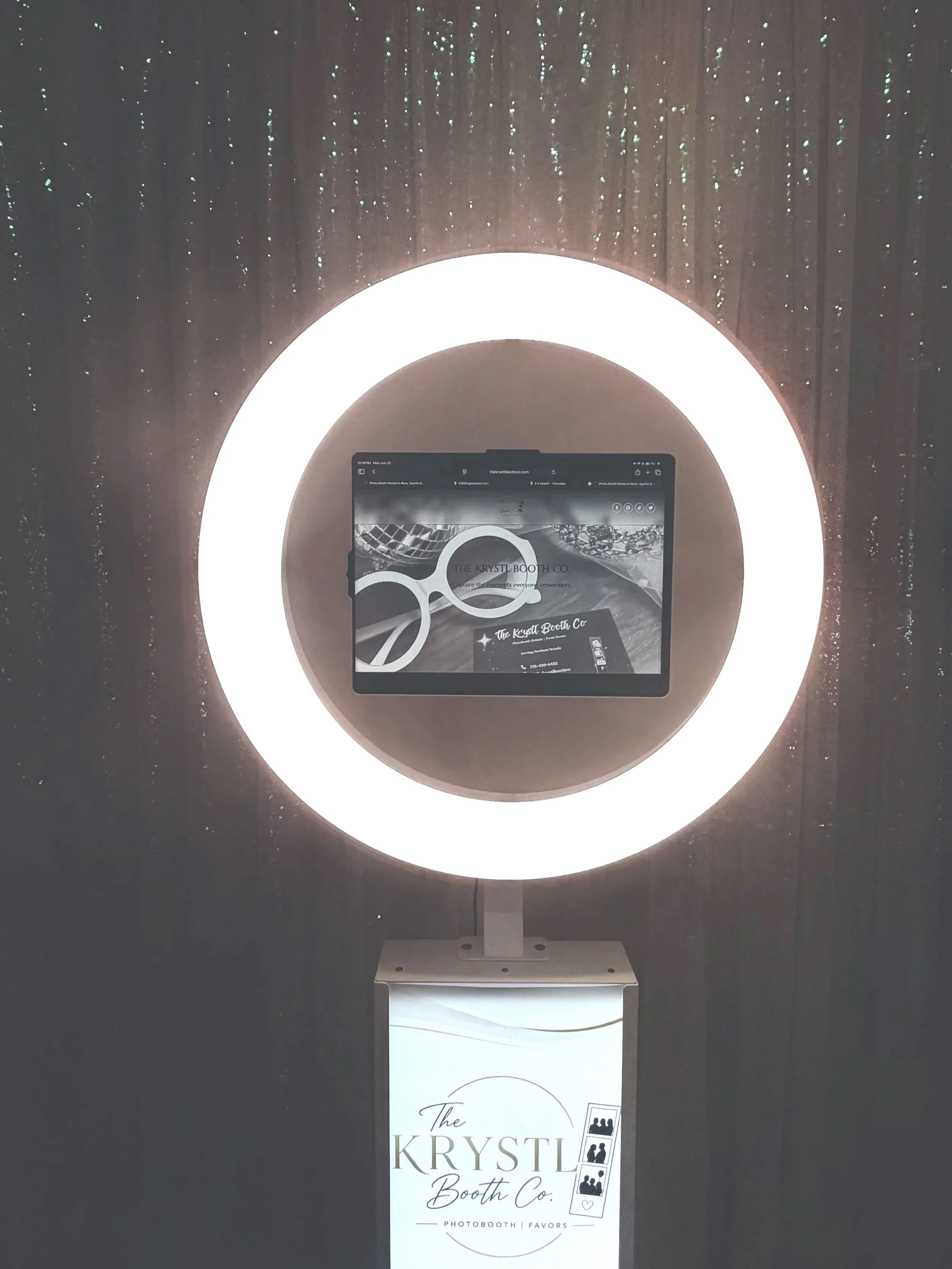 A photo booth and mirror with stylish lighting backdrop, promoting 'The Krystl Booth Co.' for photo booth and favors services.