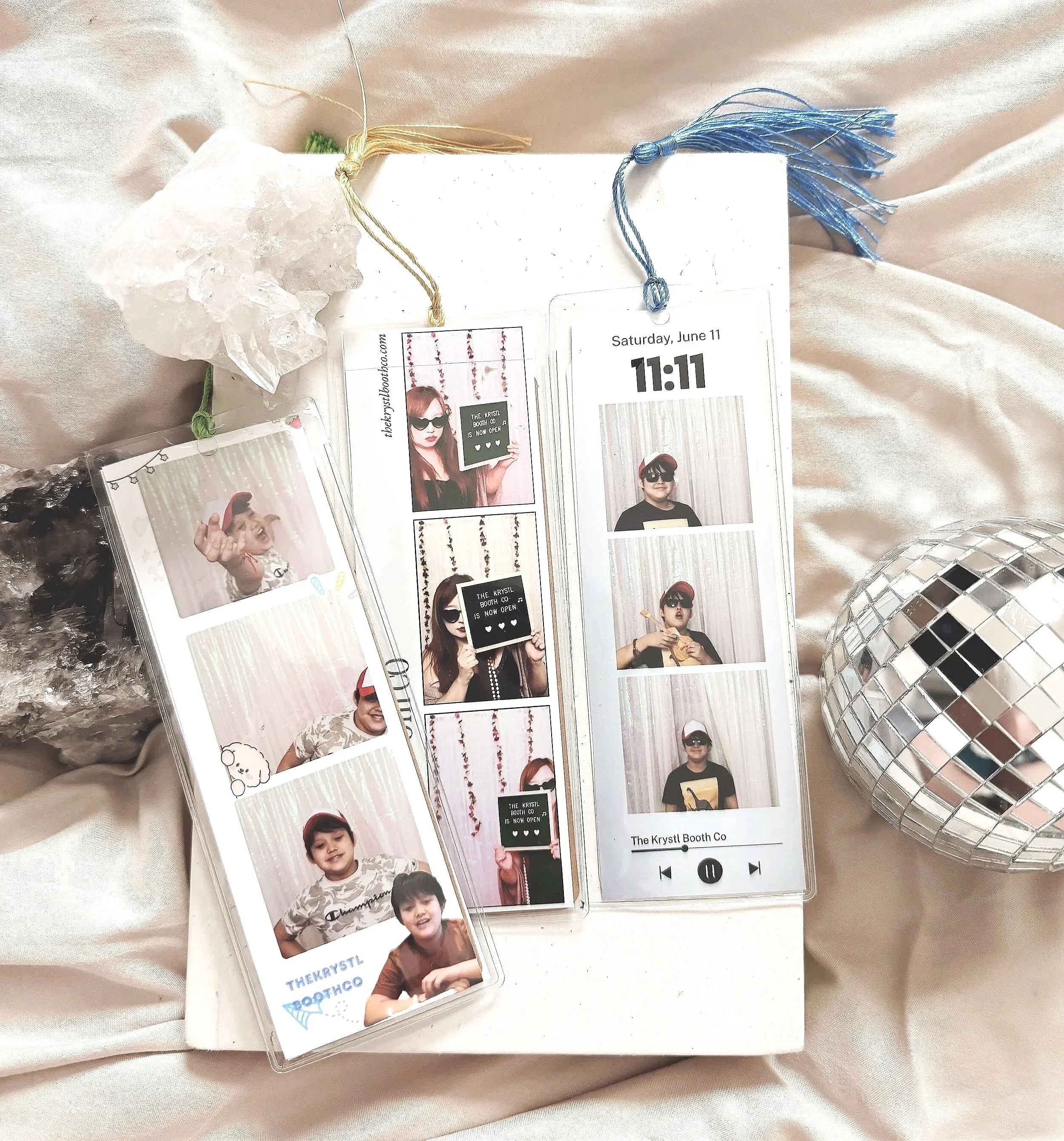 Photo of photo booth pictures of children and a ticket, with a crystal and a mirror ball in the background, resting on shiny beige fabric.