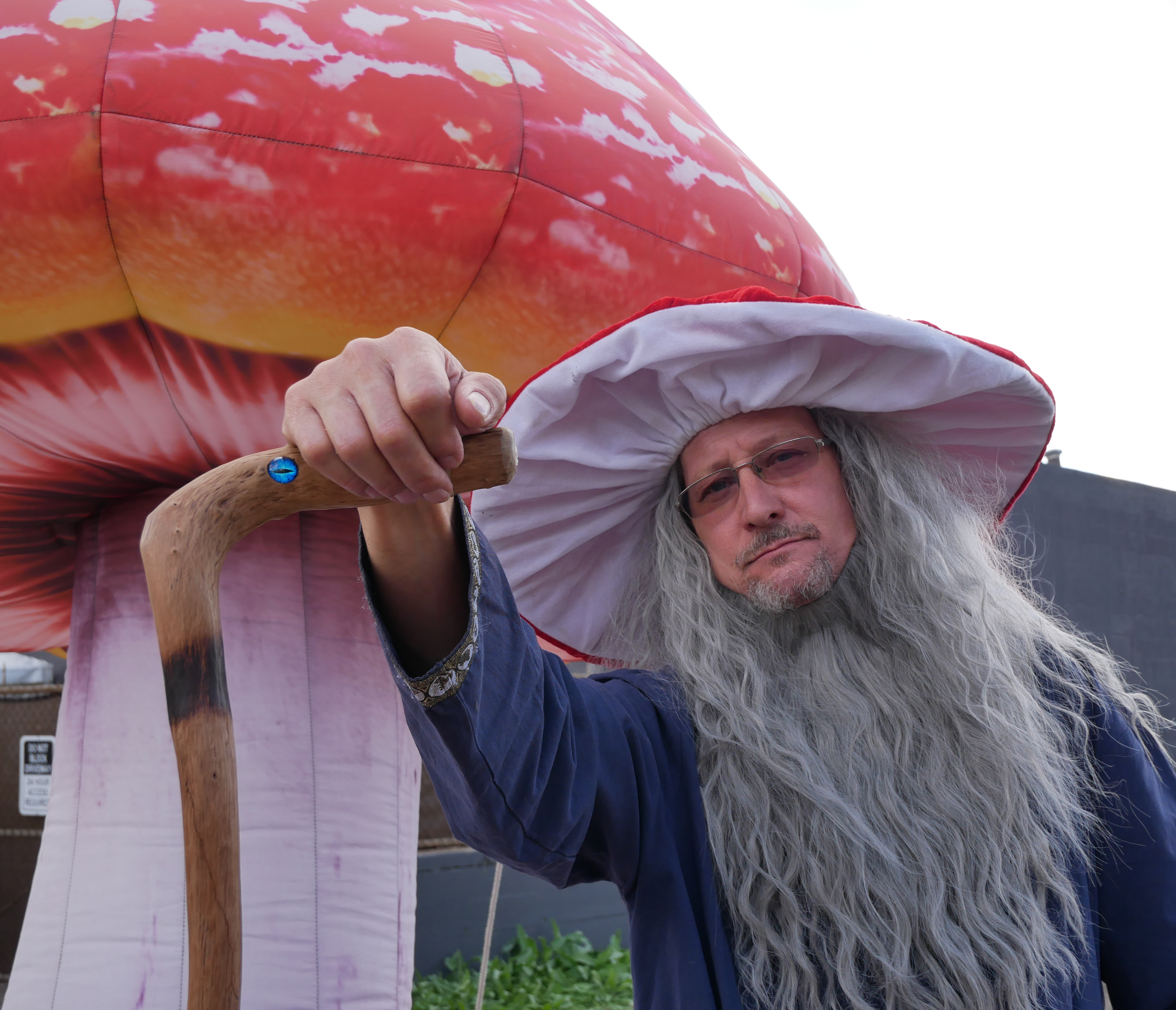 A person dressed as the Wizard of Oz's wizard, Toto the dog, with a large red and pink hot air balloon shaped like a peach puppet, and a white sky background.