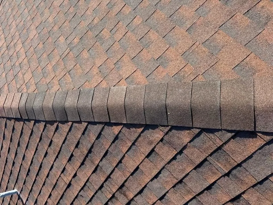 Close-up view of a roof with overlapping asphalt shingles in brown and reddish hues.