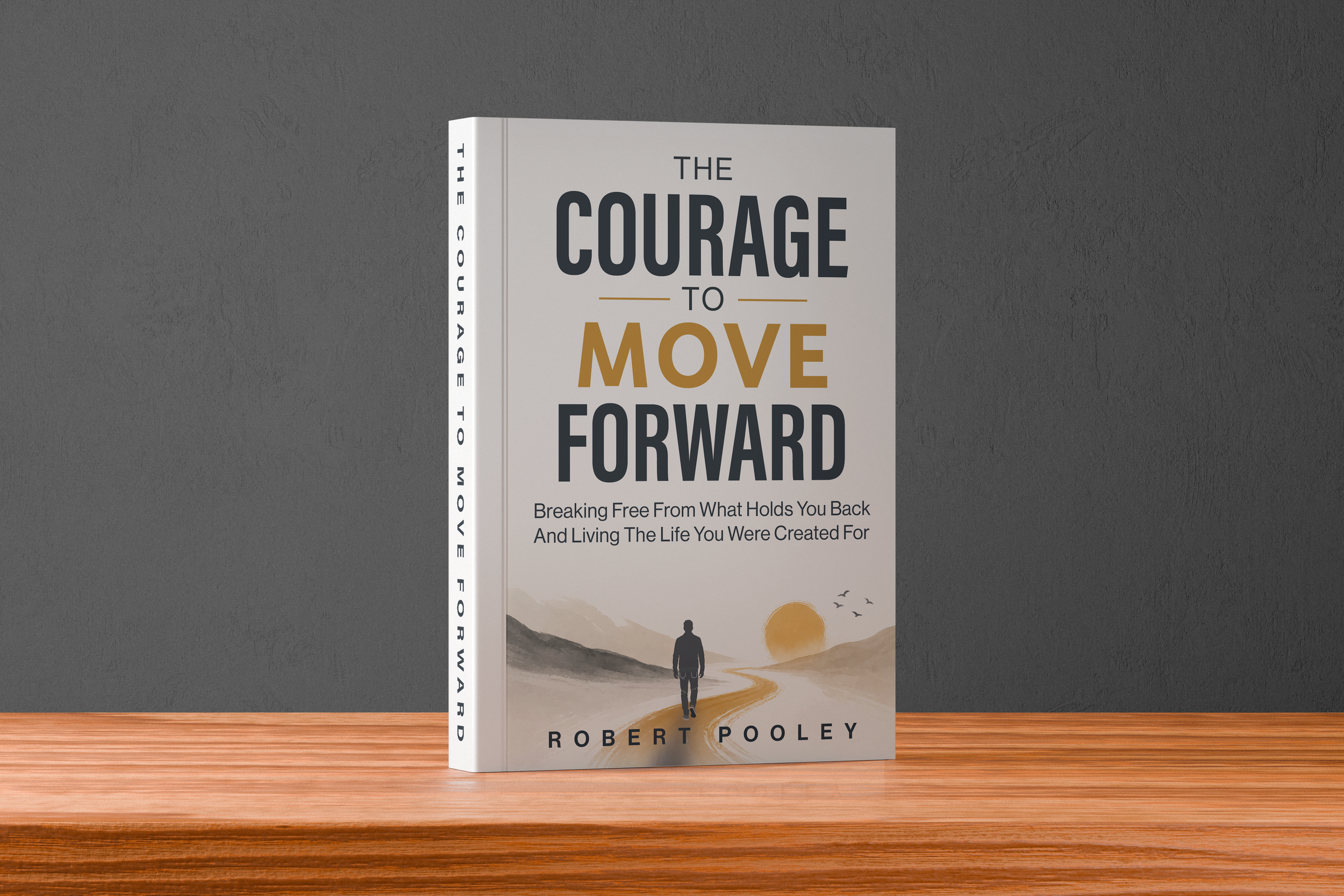 Book titled "The Courage to Move Forward" by Robert Pooley placed on a wooden surface against a gray wall, featuring a cover with a person walking towards a sunset over mountains.