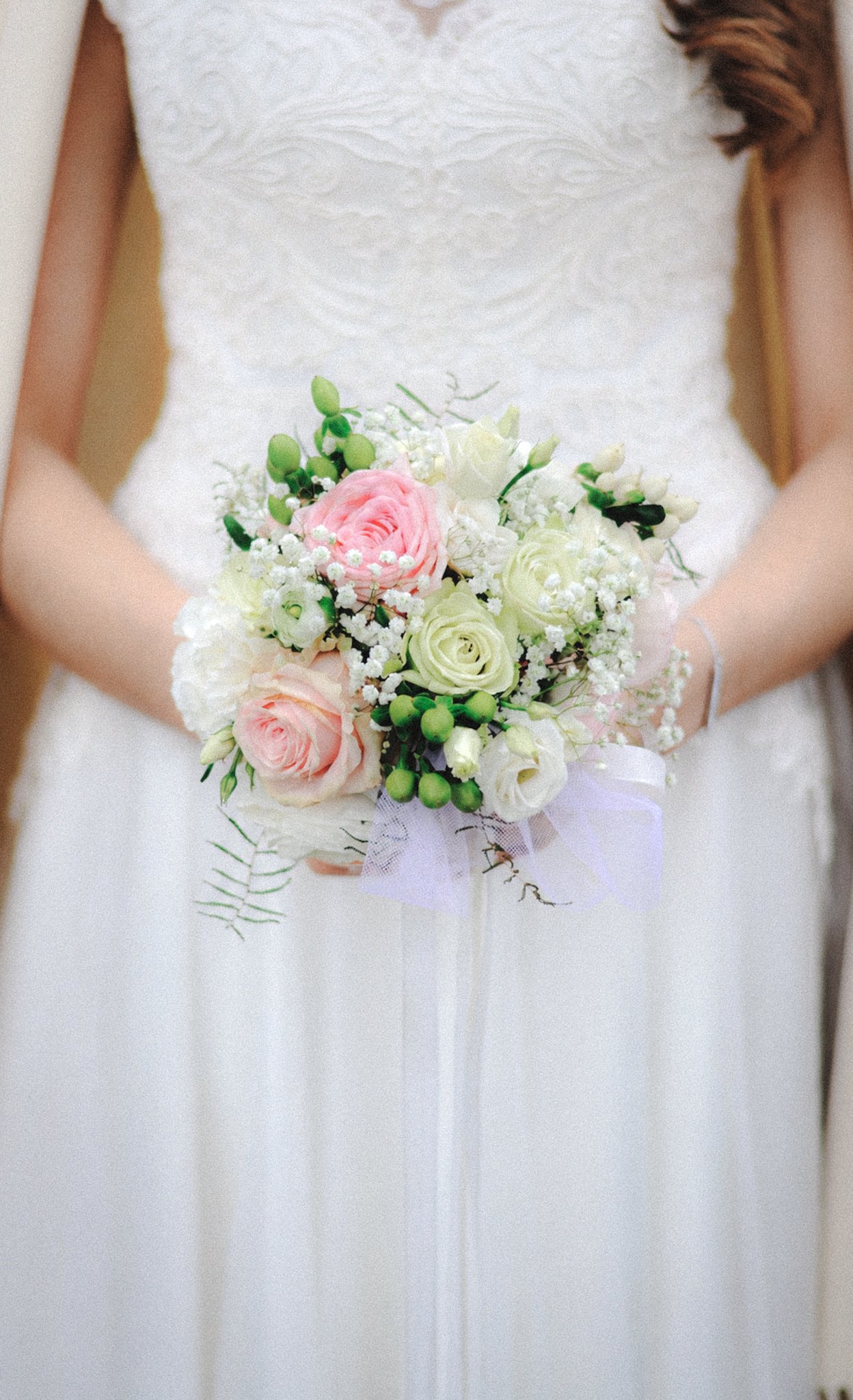 A bride in a white lace dress holding a bouquet of pink and white roses and greenery.