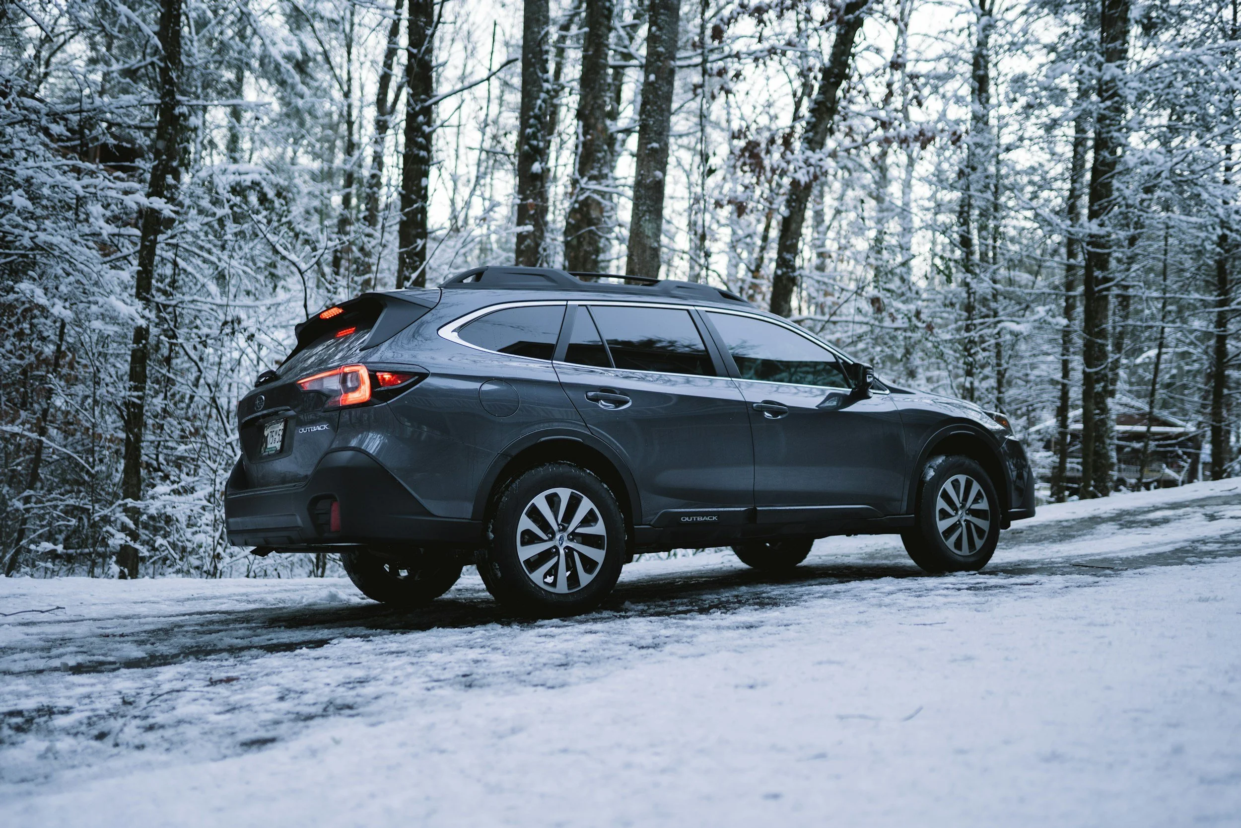 A black Subaru Outback SUV parked on a snowy road surrounded by a forest with snow-covered trees.