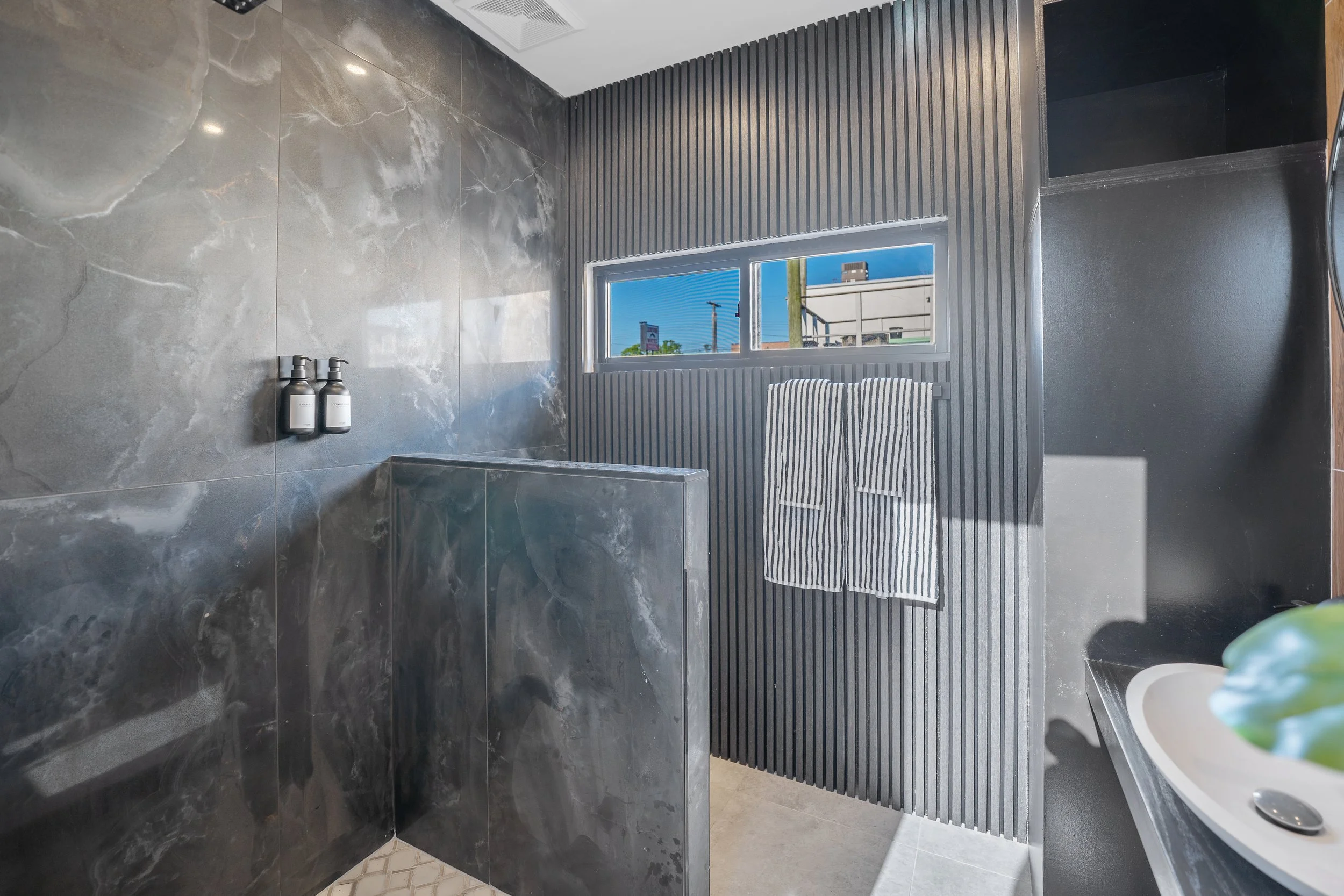 Modern bathroom with gray marble walls, a window with a view outside, a striped towel hanging, and black wood paneling.