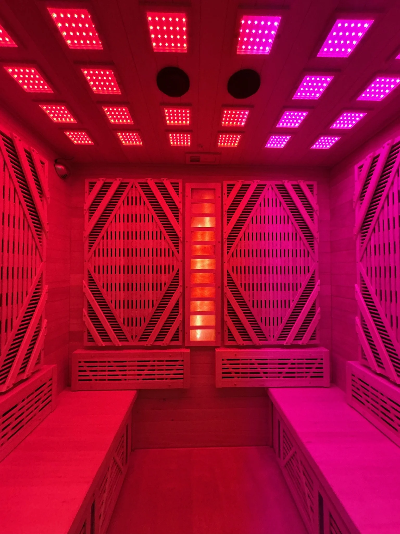 Sauna room with lavender and red LED lighting, wooden benches on both sides, and wooden slats on the walls.