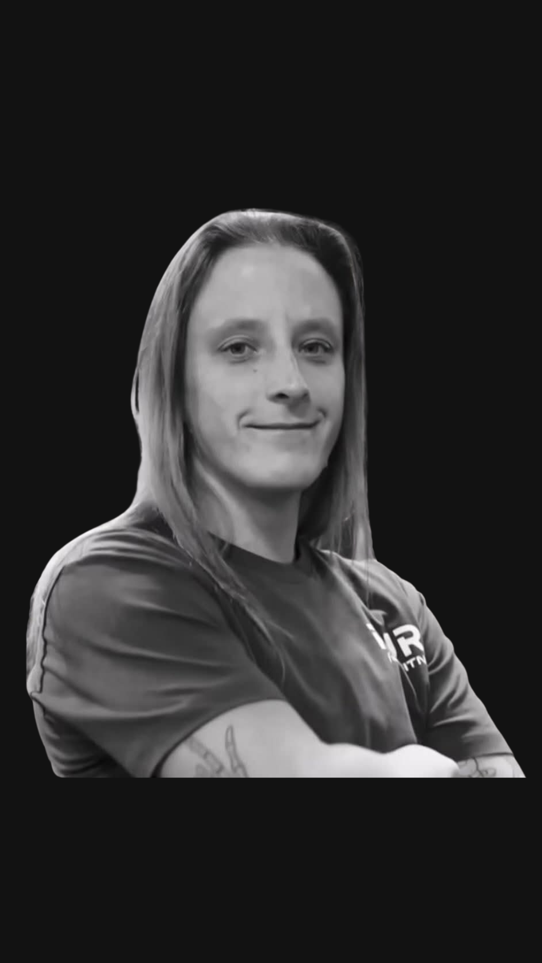 Black and white photo of a woman with long hair, smiling slightly, wearing a sports shirt with arms crossed, against a black background.