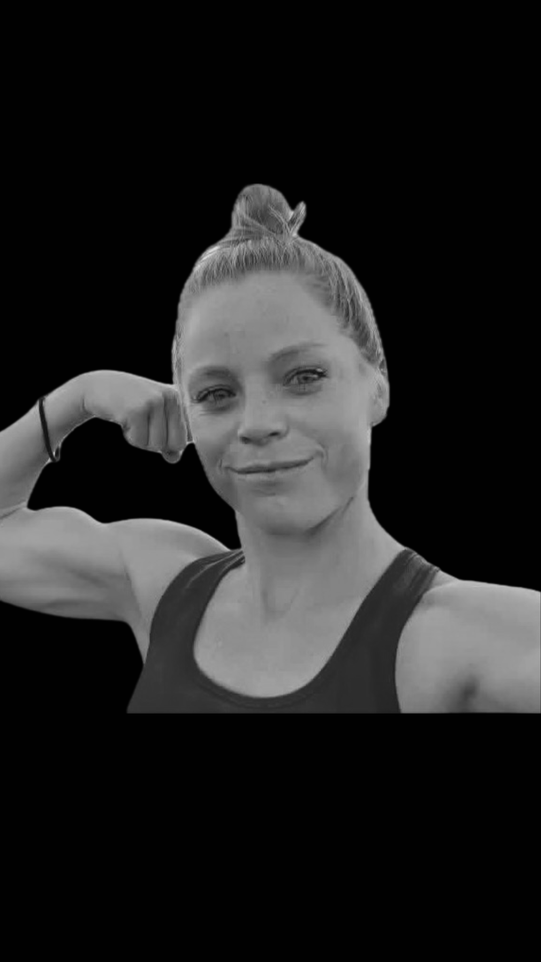 Black and white photo of a woman with her hair in a bun, smiling and flexing her right arm, wearing a tank top, with a solid black background.