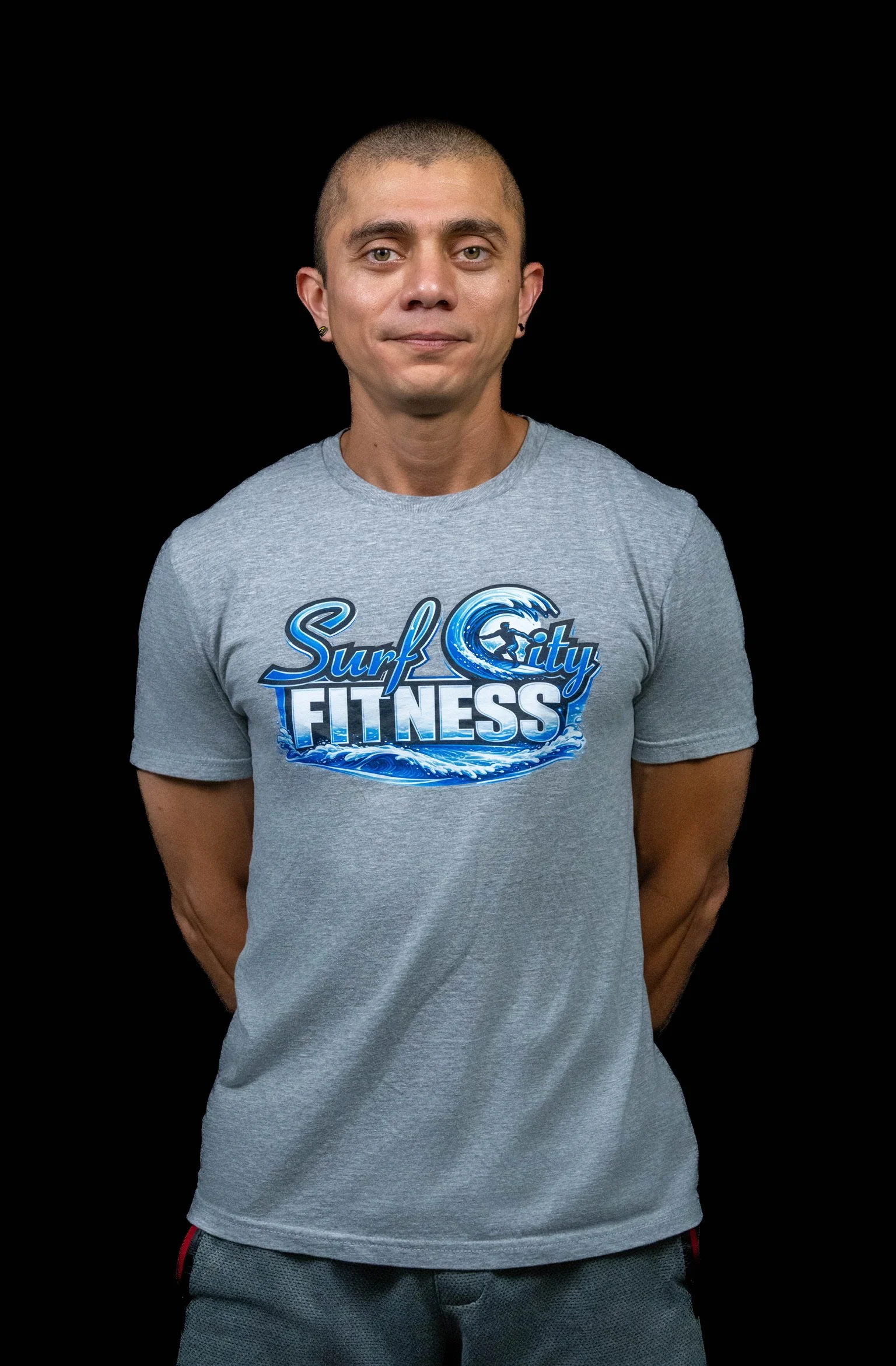 Man in a gray t-shirt with 'Surf City Fitness' logo, standing against black background.