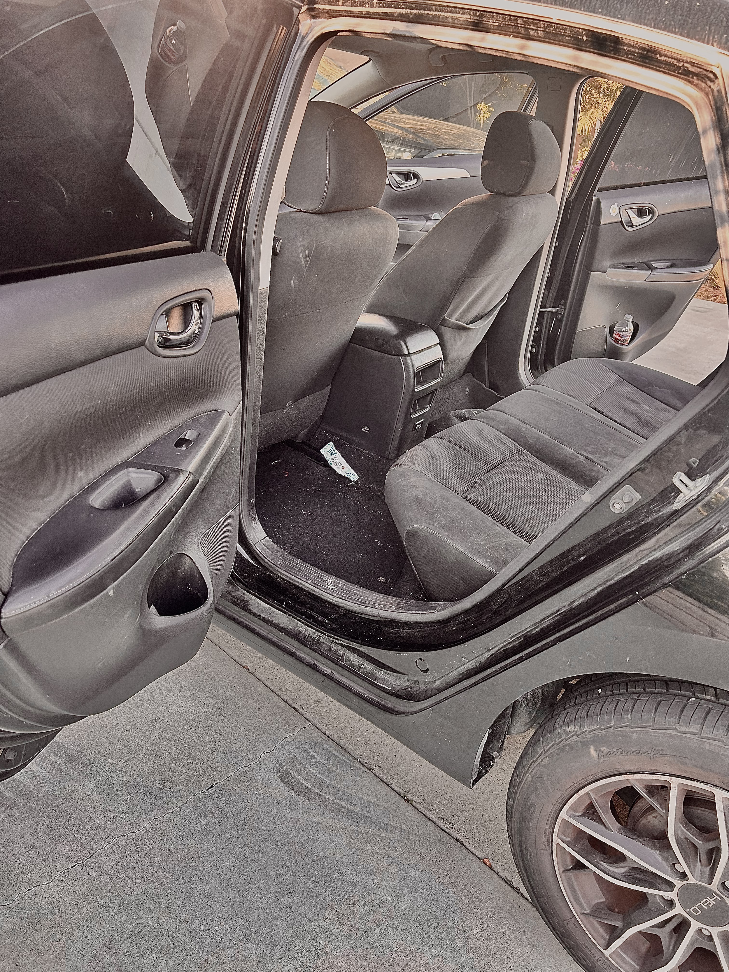 Interior view of a black car showing the front and back seats, door panels, and the floor. The car appears to be parked in a garage or parking lot.